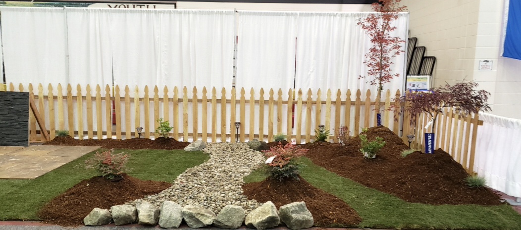 Garden with a wooden fence, gravel pathway, and landscaped flower beds with plants and rocks.