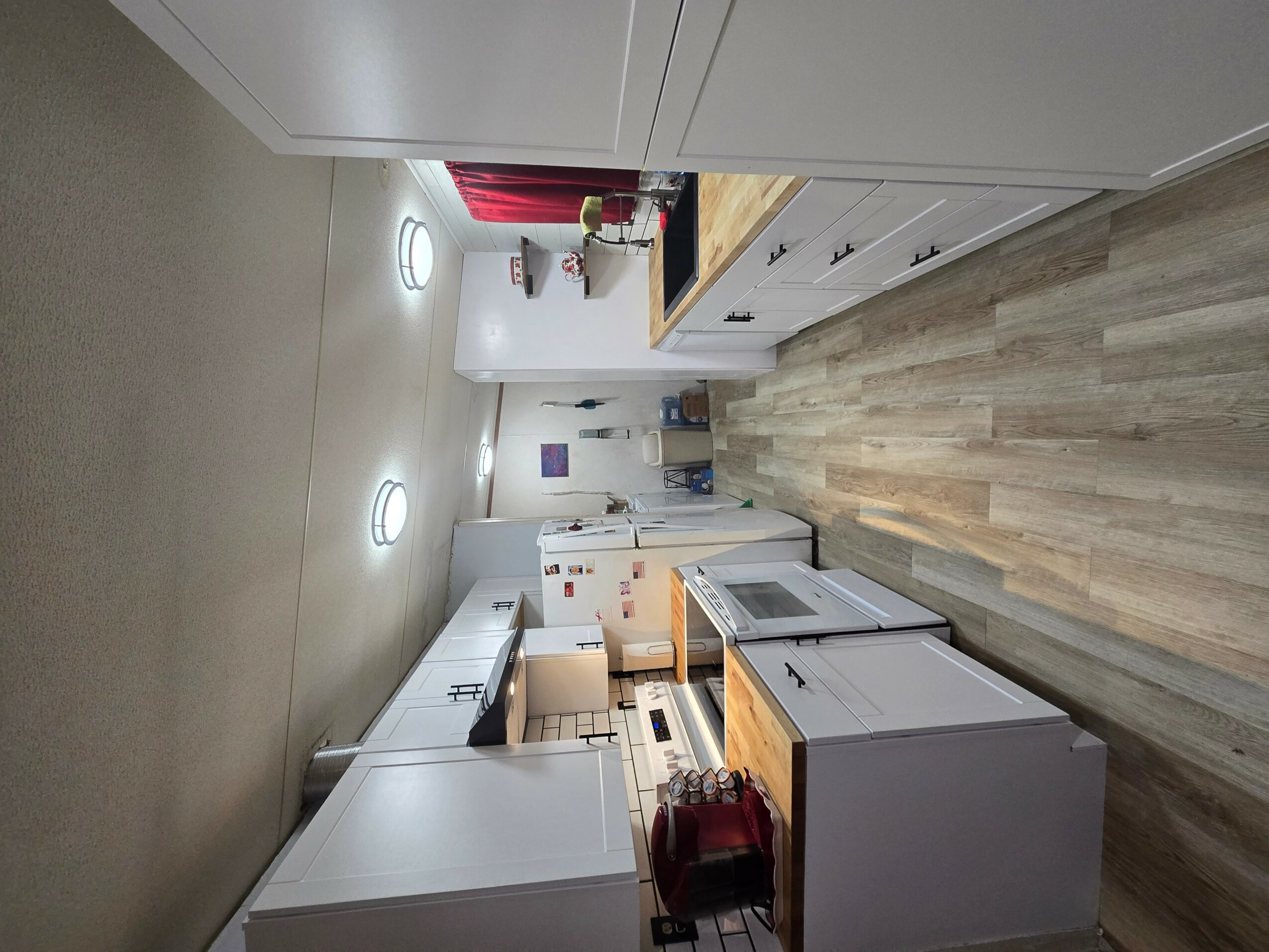 Kitchen with white cabinets, wooden countertops, and appliances including a microwave and refrigerator. Light wood flooring and ceiling lights.