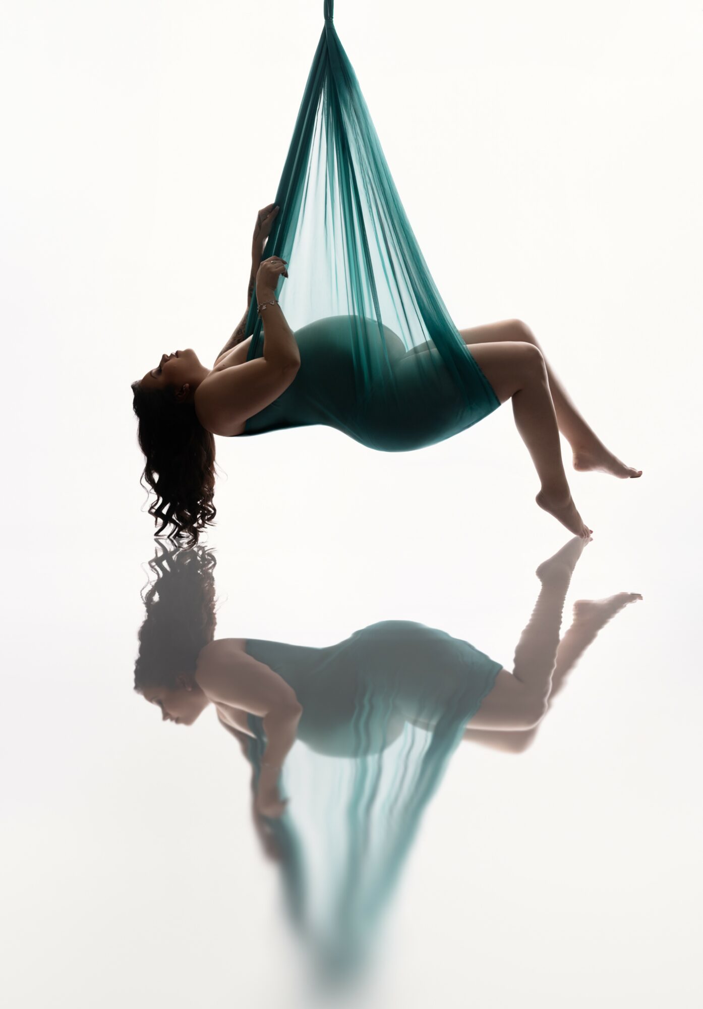 Person lying in a hammock, hanging upside down, with their reflection visible on a shiny surface below.