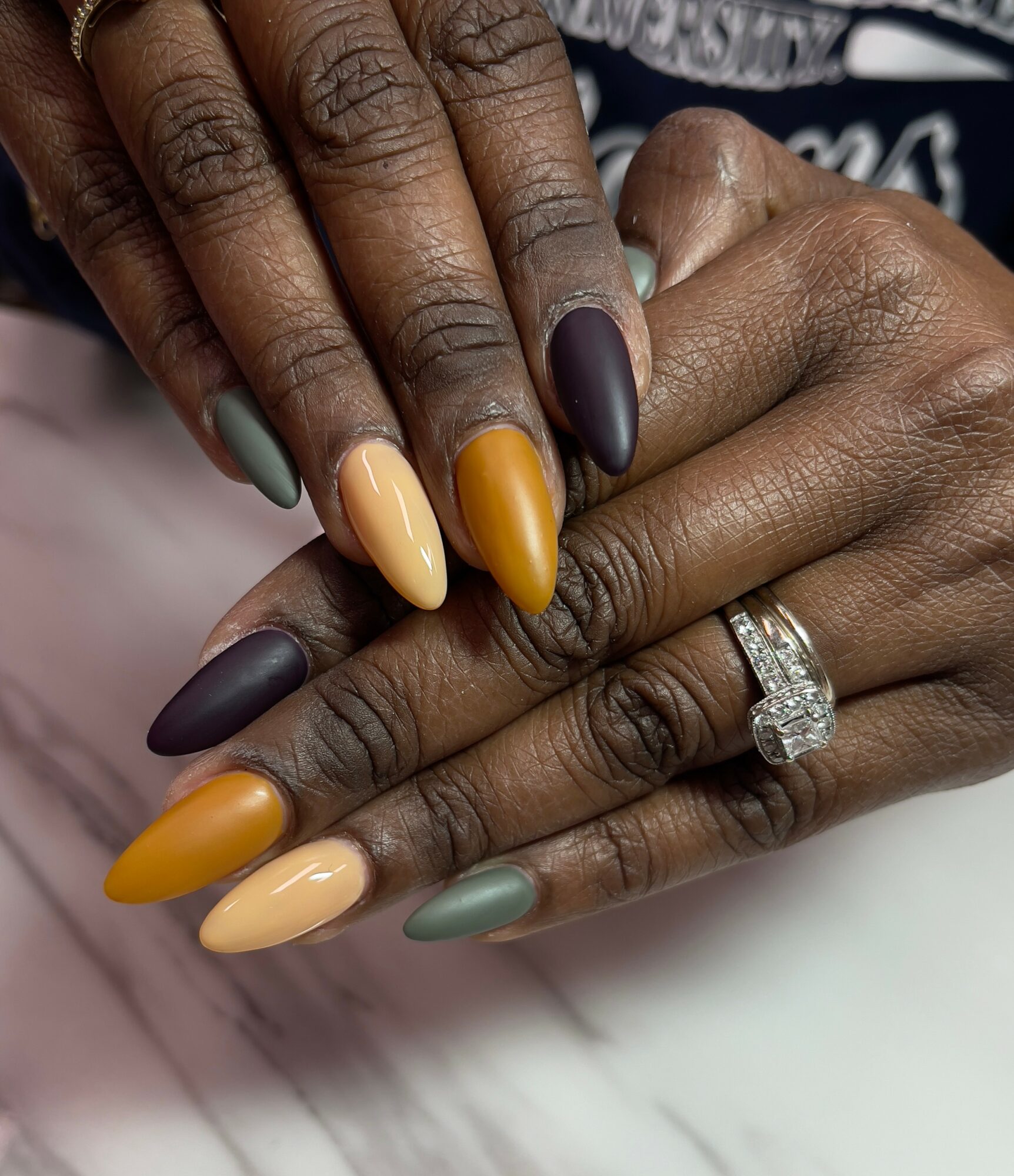 Two hands with colorful manicured nails, one hand has a diamond ring, resting on a white surface.