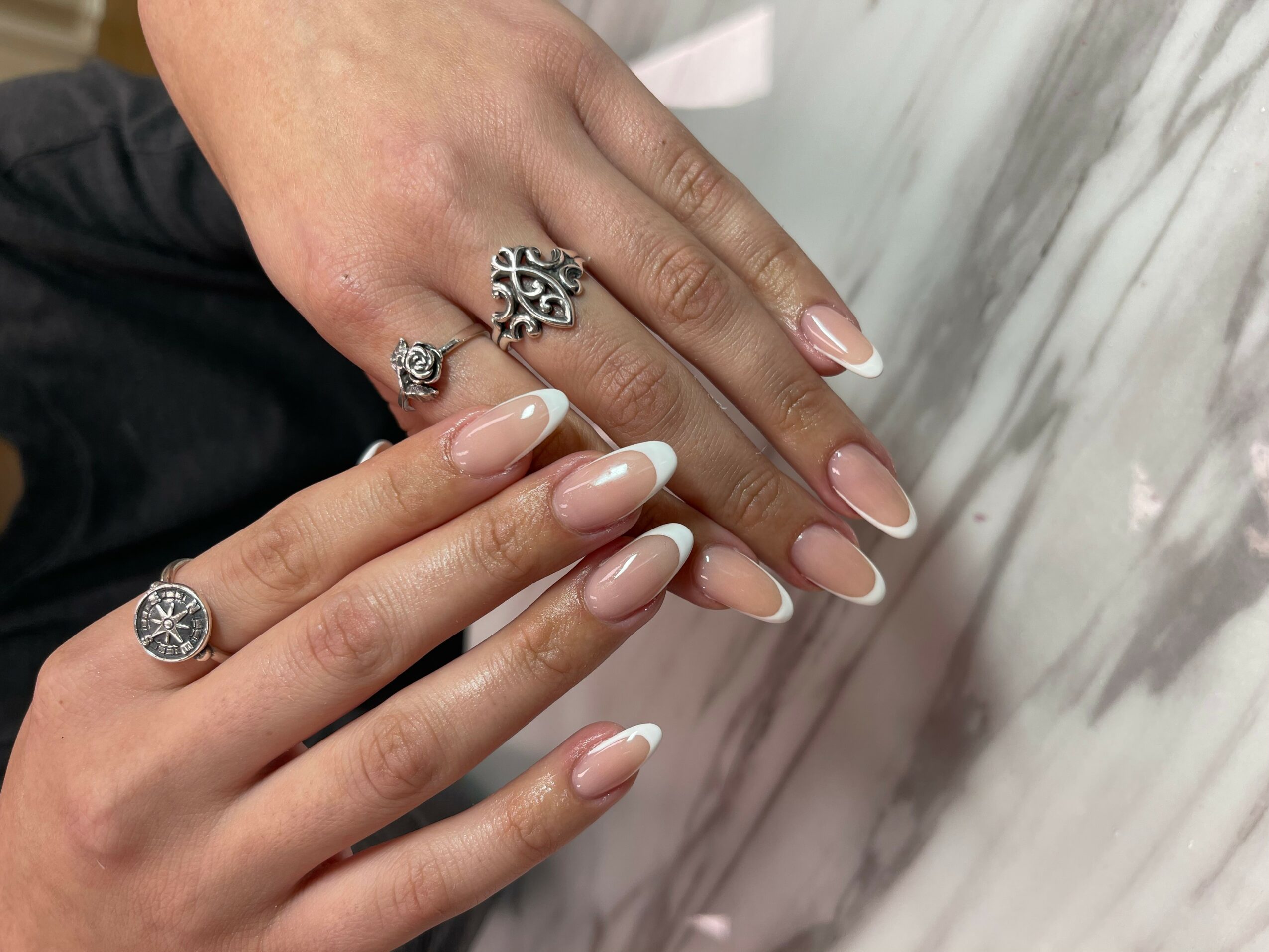 Two hands with manicured nails and multiple rings, resting on a marble surface.