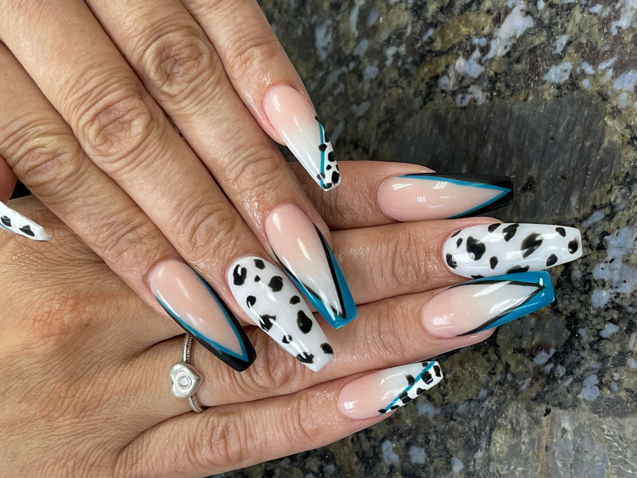Hand with long, almond-shaped nails featuring black and white spotted and striped designs, on a textured surface.