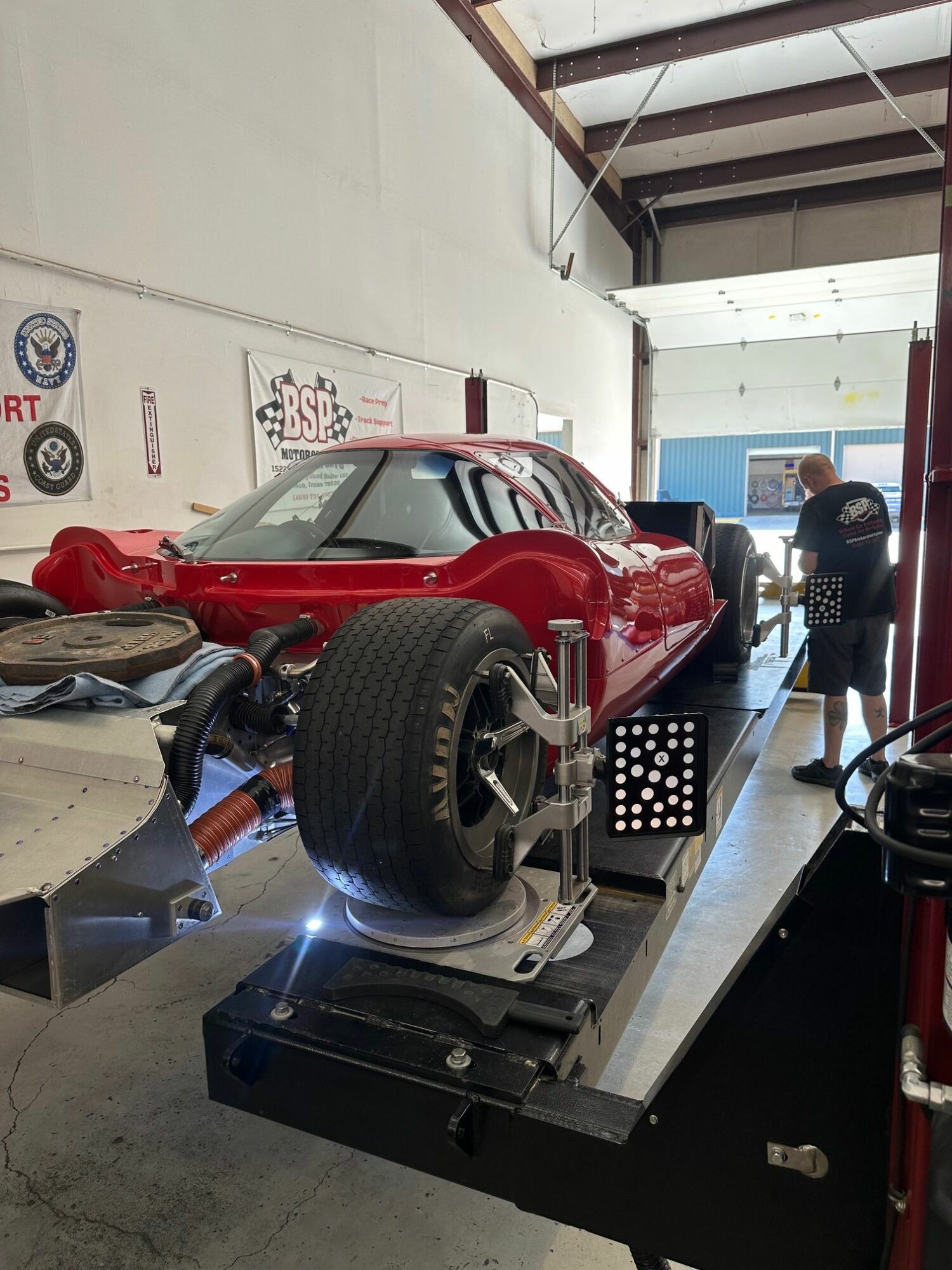 Red race car on testing platform inside garage with two people working nearby.