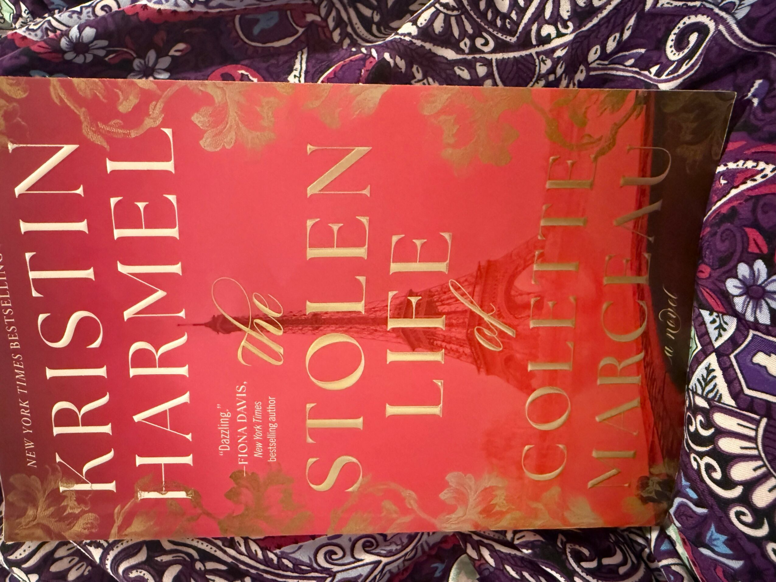 Book cover titled 'Christin the Charmel' with red background and gold text, placed on patterned fabric.