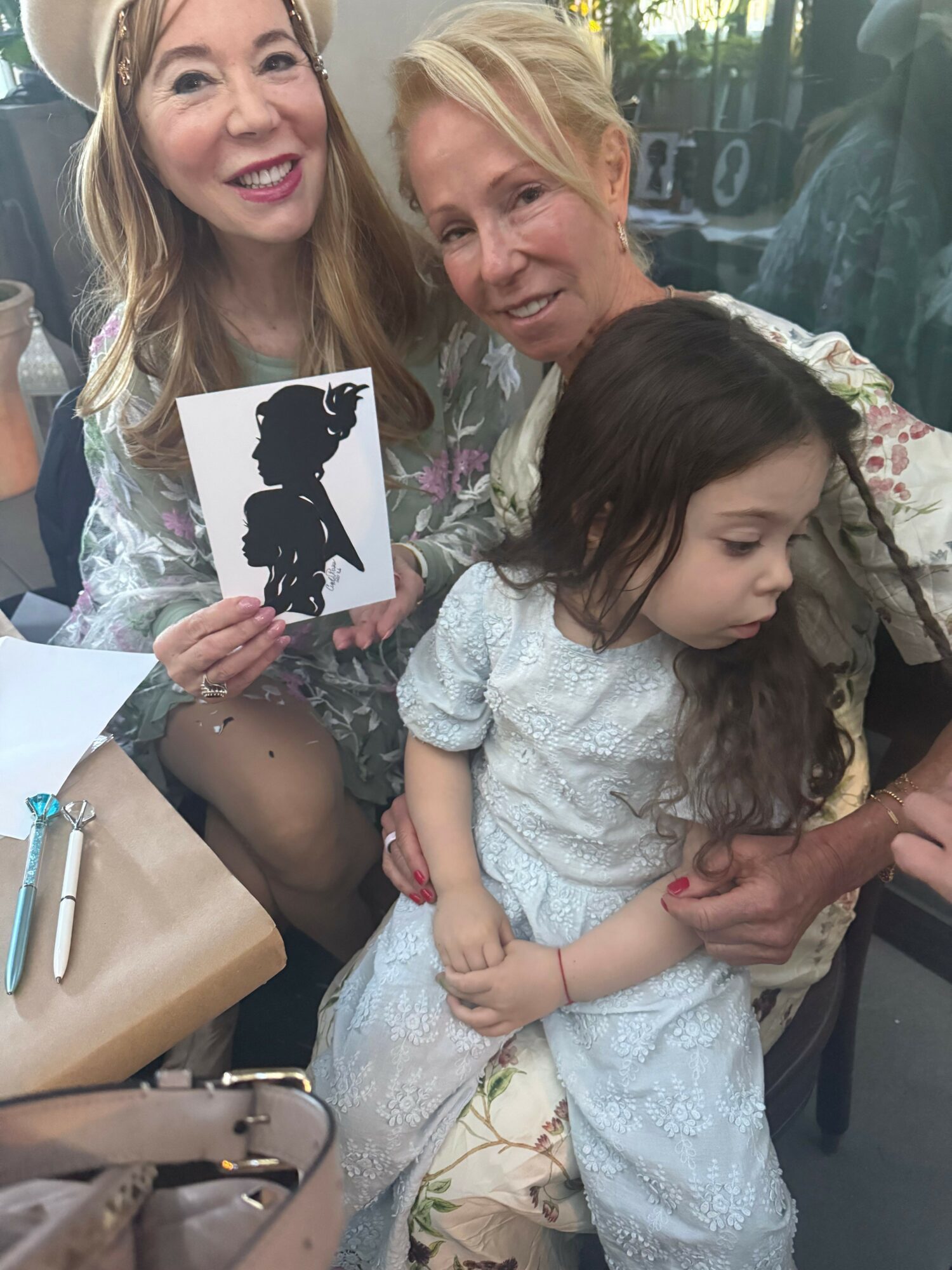 Three women and a girl sitting together, one woman holding a silhouette cutout, in a casual setting.