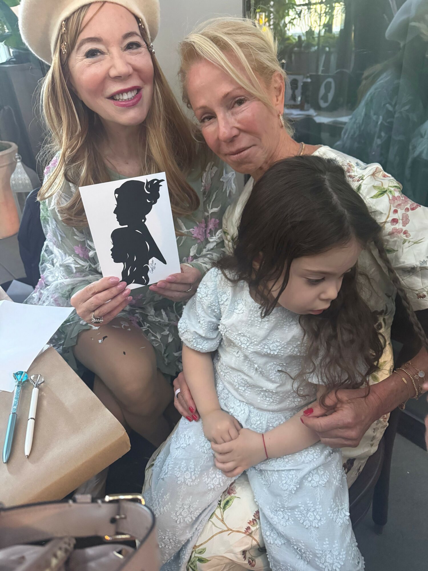 Three women and a girl sitting together, one woman holding a silhouette cutout, in a casual setting.
