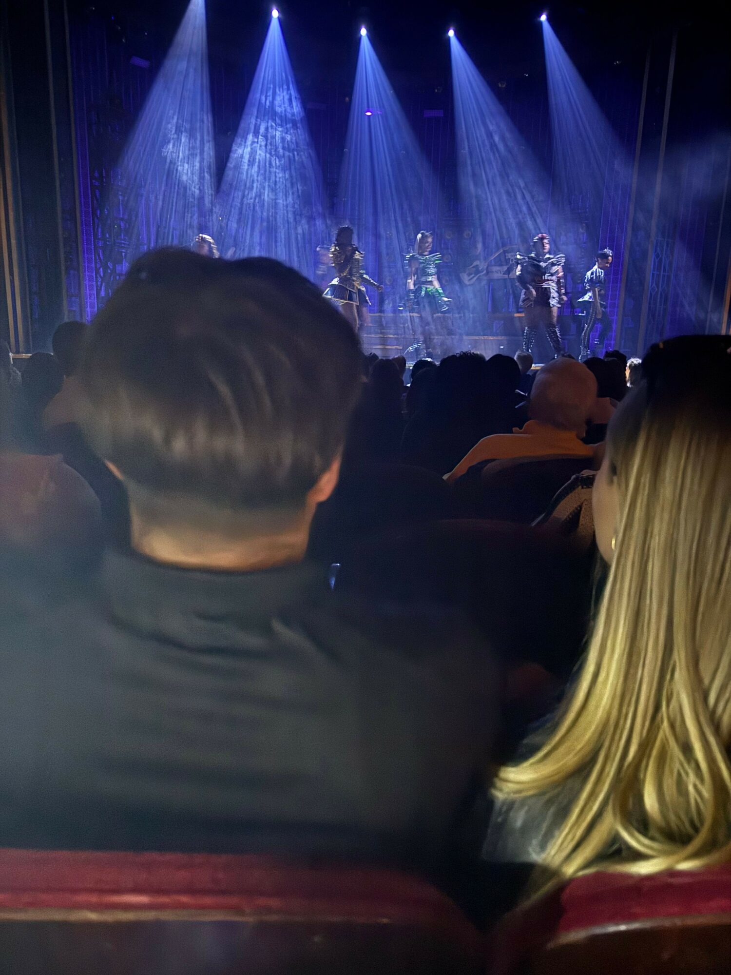 Audience watching a stage performance with performers under blue and purple lighting.