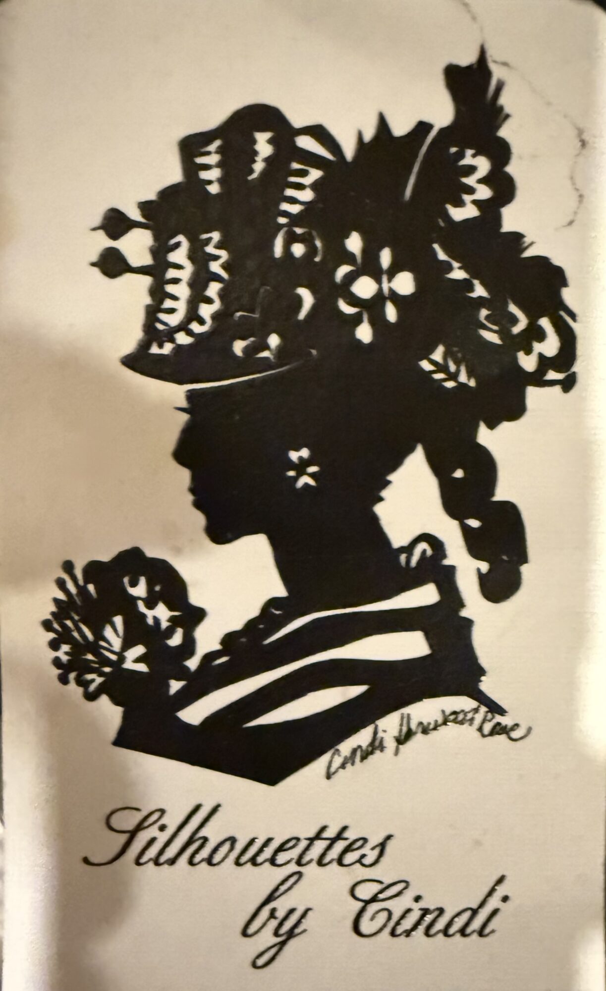Silhouette of a woman with an elaborate hairstyle and a flower, holding a fan, with text 'Silhouettes by Cindi'.