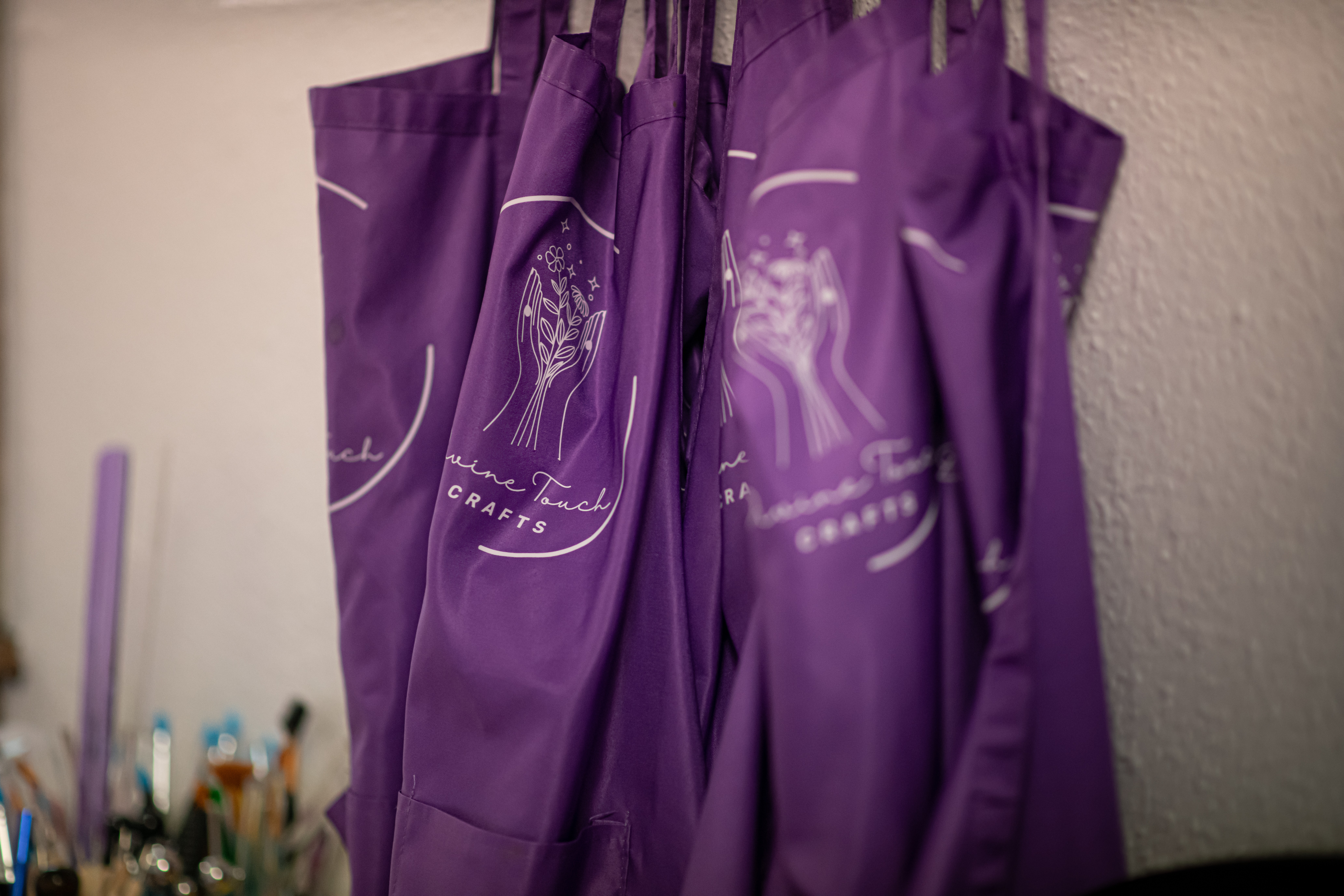 Multiple purple bags hanging on hooks against a wall, with art supplies visible in the background.