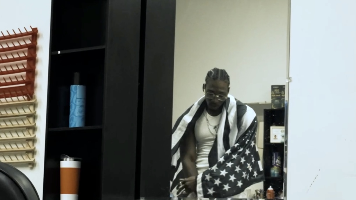 Person with glasses and a towel over shoulders, holding a bag with stars, in a room with shelves and bottles.