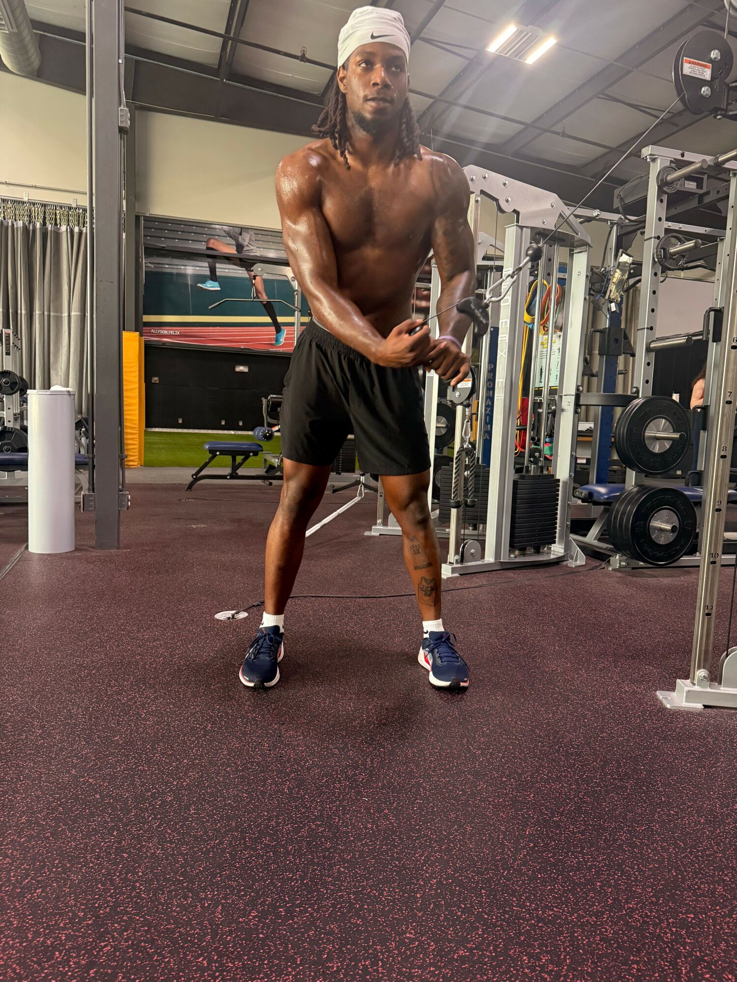 Muscular man in black shorts and sneakers standing in gym with equipment in background.