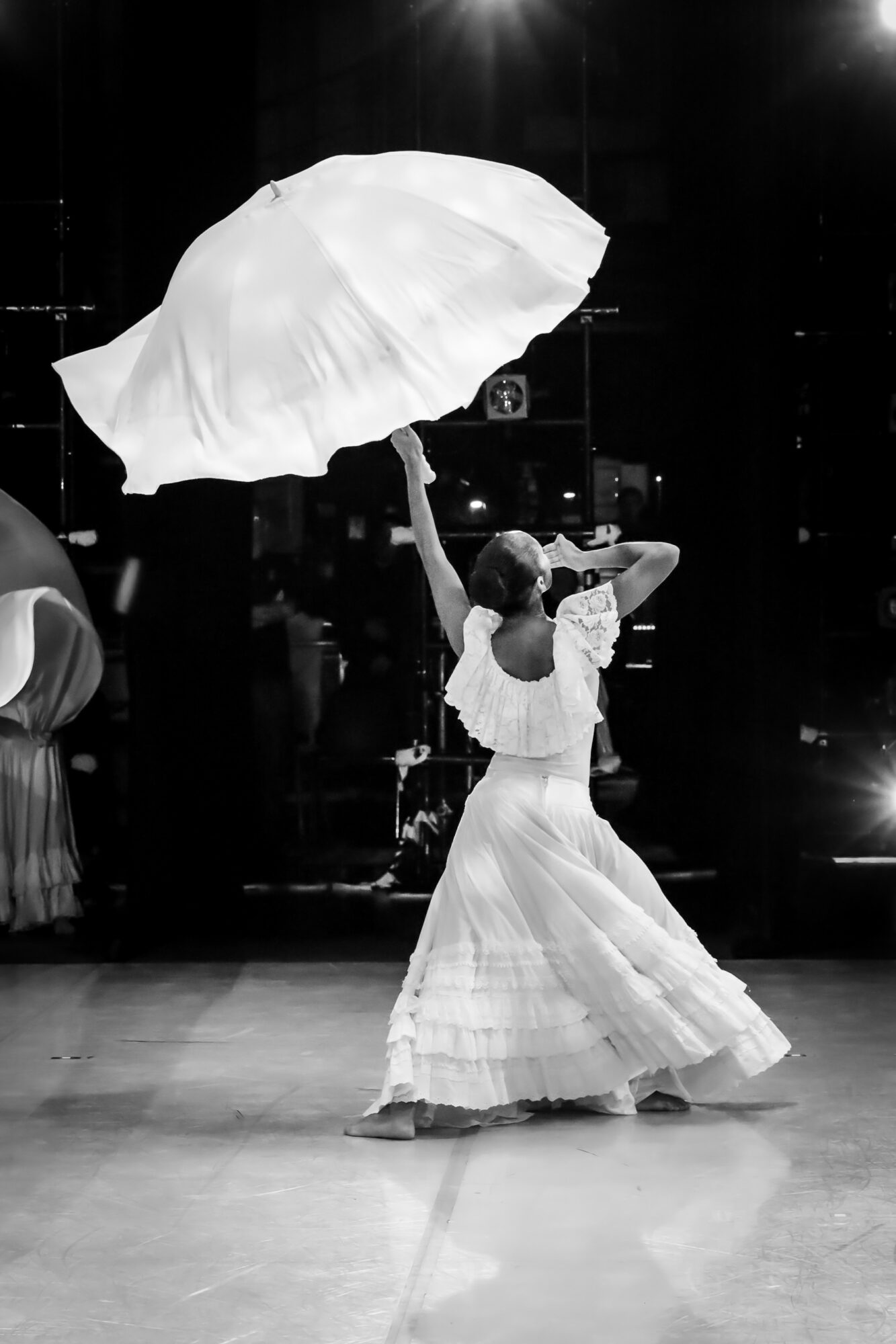 Person in a long dress holding an umbrella, dancing indoors with a dark background.