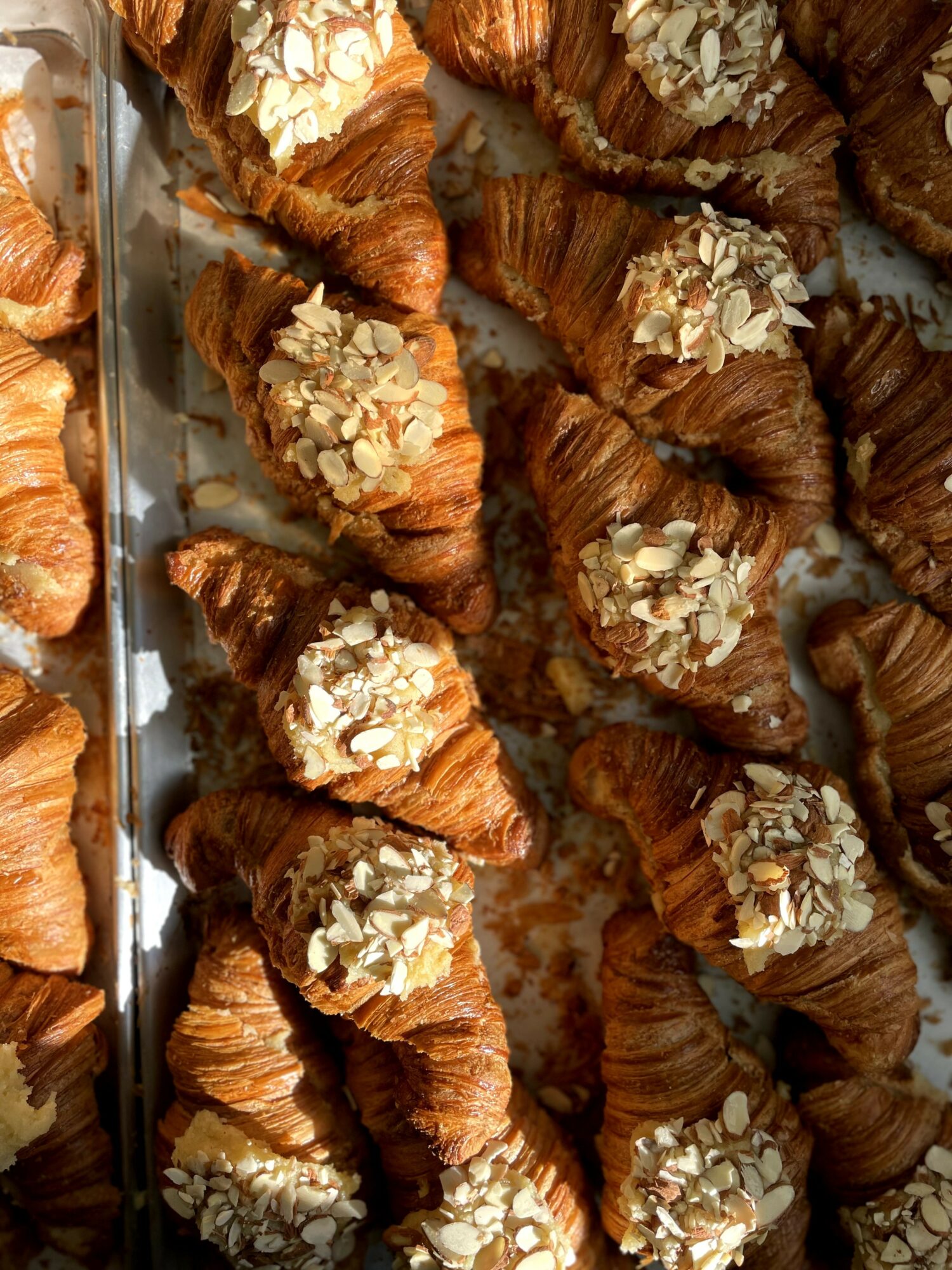 Multiple croissants topped with sliced almonds arranged on a tray, some overlapping each other.