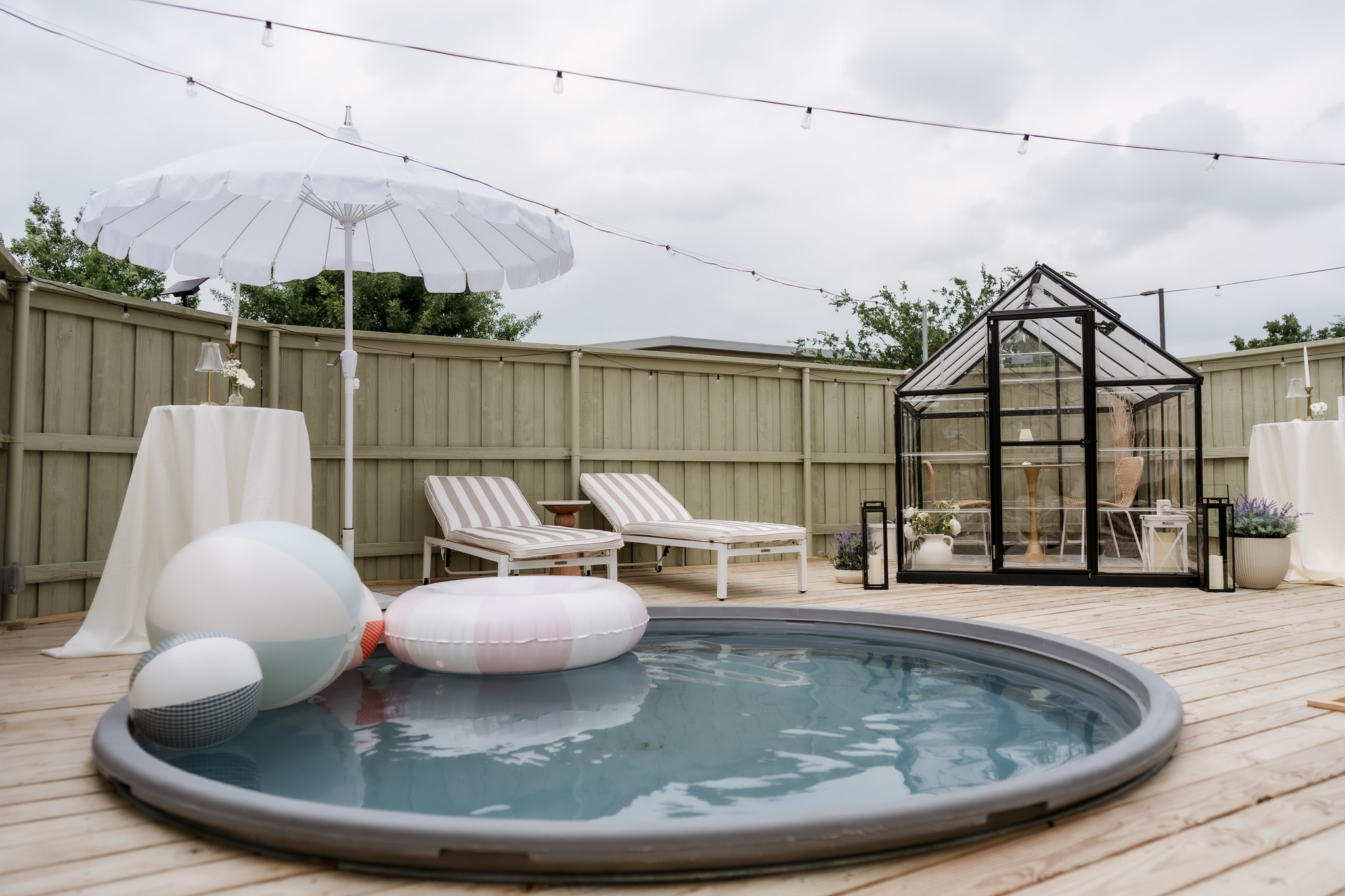 Outdoor pool area with lounge chairs, a greenhouse, and pool floats under a cloudy sky.