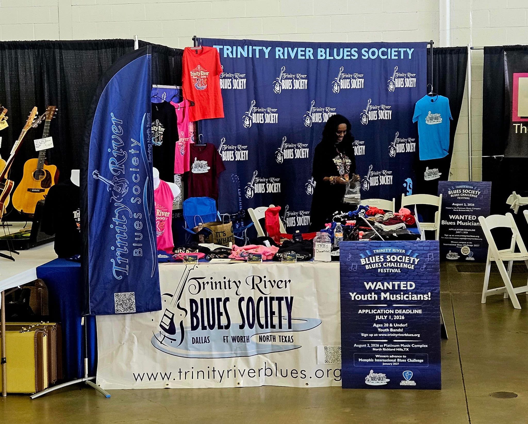 Booth for Trinity River Blues Society with banners, tables, and a person standing behind the table.
