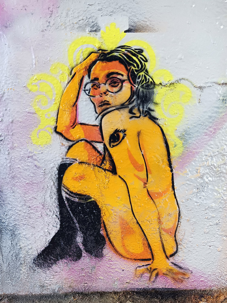 Street art of a woman with glasses, sitting with one arm on her head, painted on a wall with yellow and black colors.