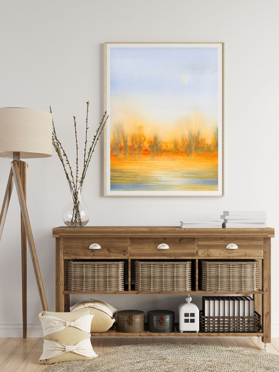 Wooden sideboard with baskets, a lamp, and decorative items, a framed landscape painting above, and a vase with branches nearby.
