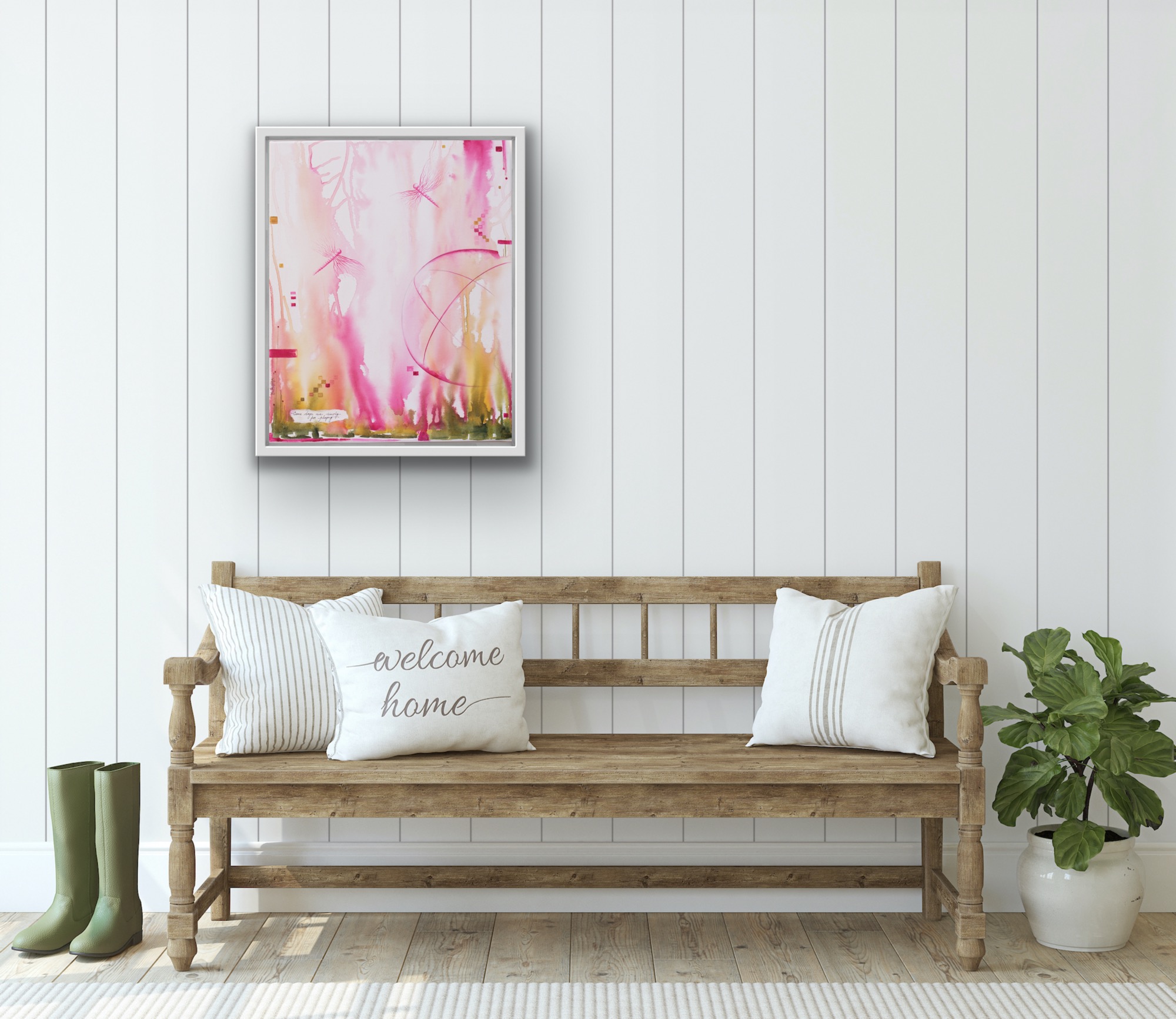 Wooden bench with three pillows, a potted plant, and a framed pink abstract artwork on a white wall, with green rain boots nearby.