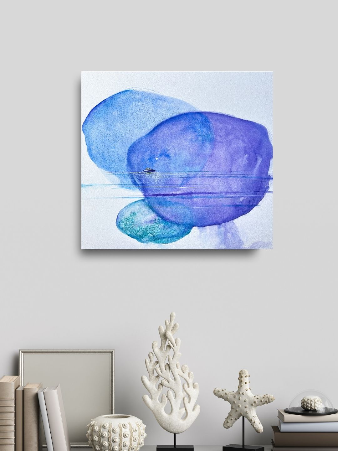 Abstract watercolor painting with blue and purple blobs on white background, hung on a wall above a decorative sculpture and starfish.