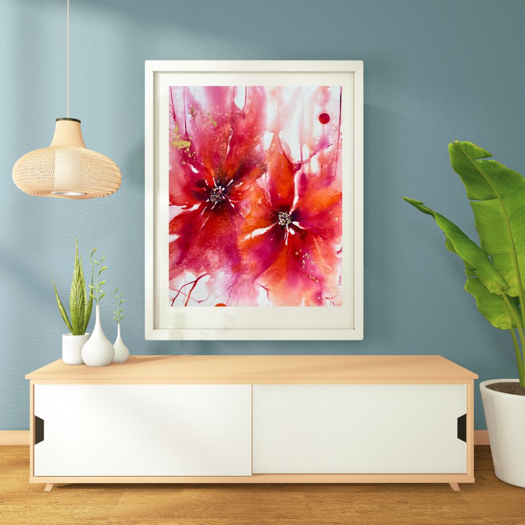 Framed abstract pink and red watercolor painting on a blue wall above a white and wood sideboard, with potted plants nearby.