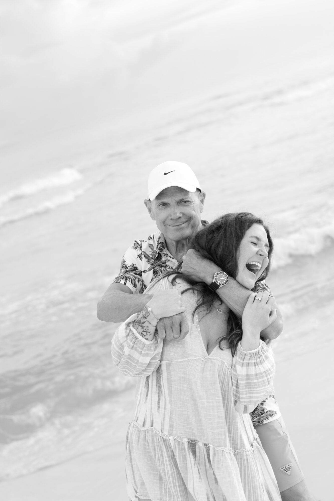 Person giving a piggyback ride to a smiling girl on a beach, ocean waves in background.