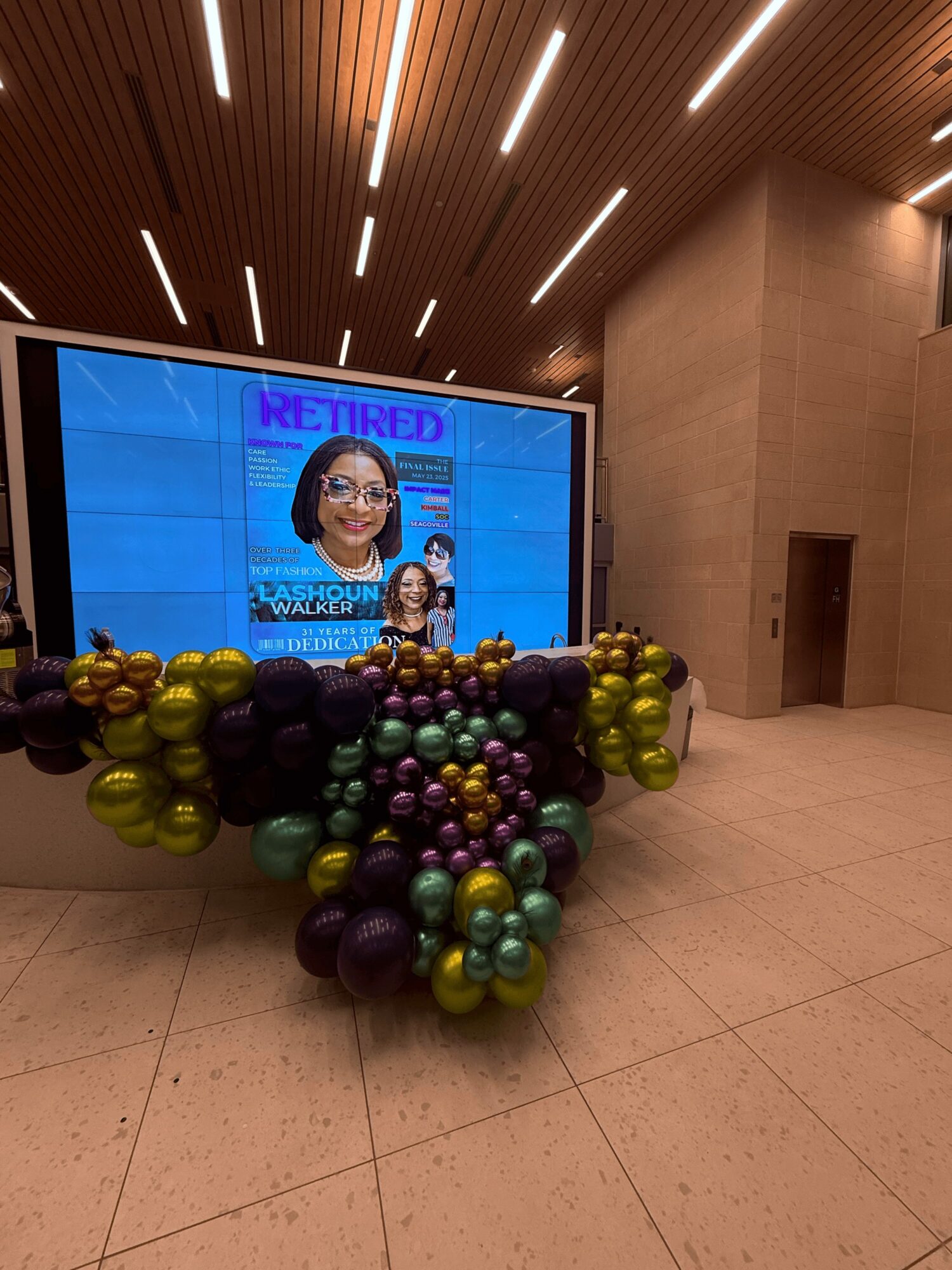 Large digital screen displaying a magazine cover with two women, surrounded by colorful balloons on the floor, in a modern interior.