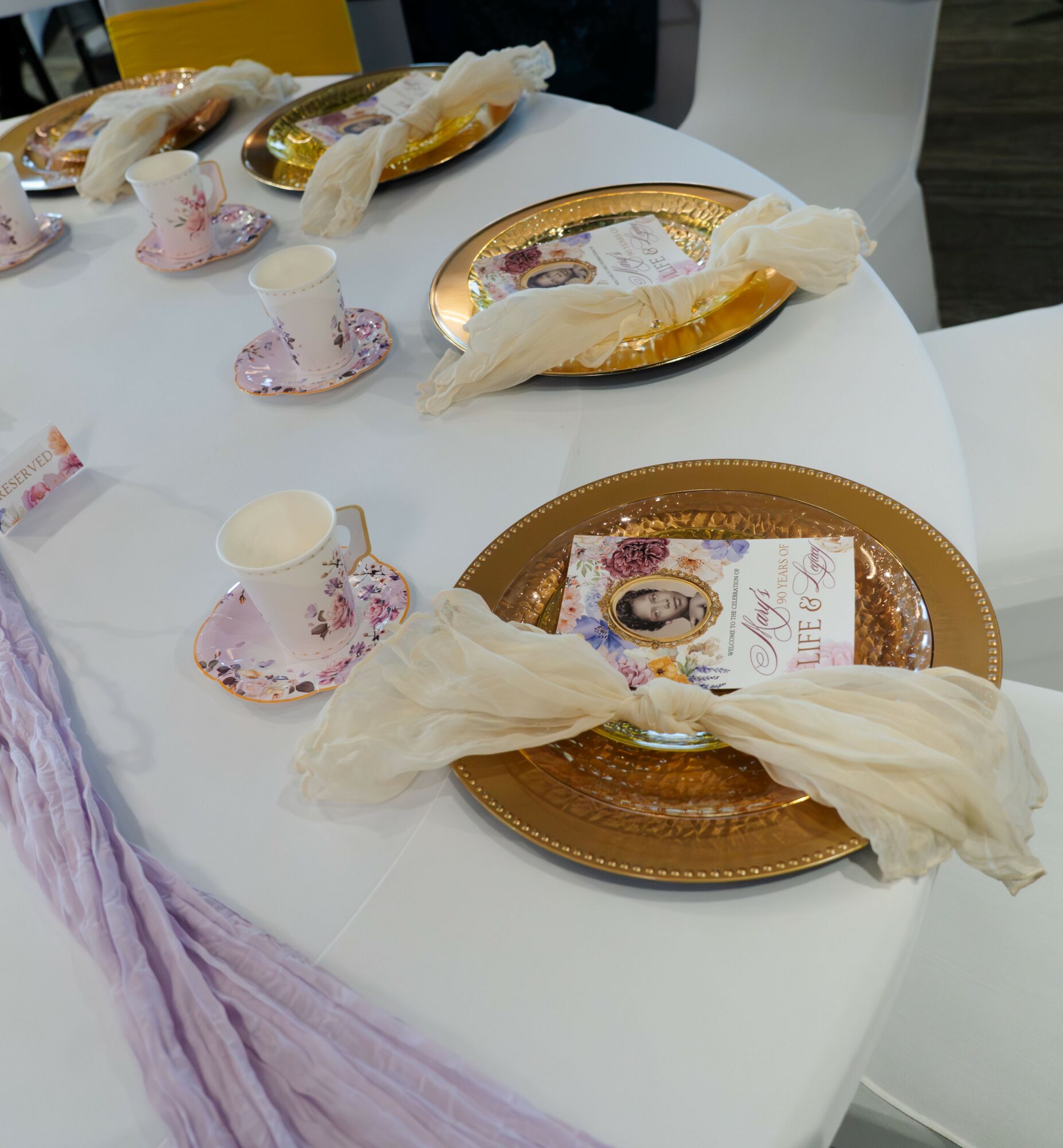 Table set with gold and pink plates, teacups, and napkins, with wrapped bread and a magazine on the table.