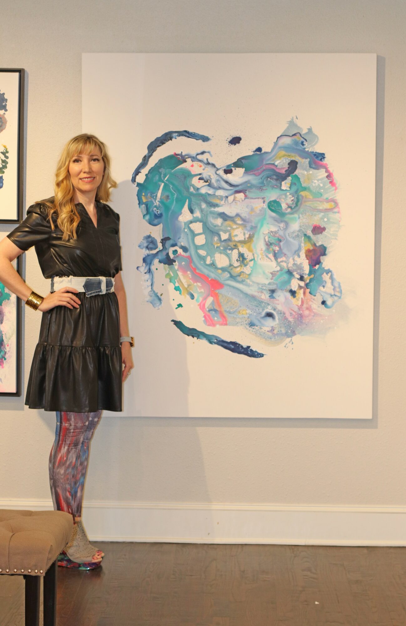 Woman with long hair in a black dress and colorful tights stands next to an abstract painting on a white wall.