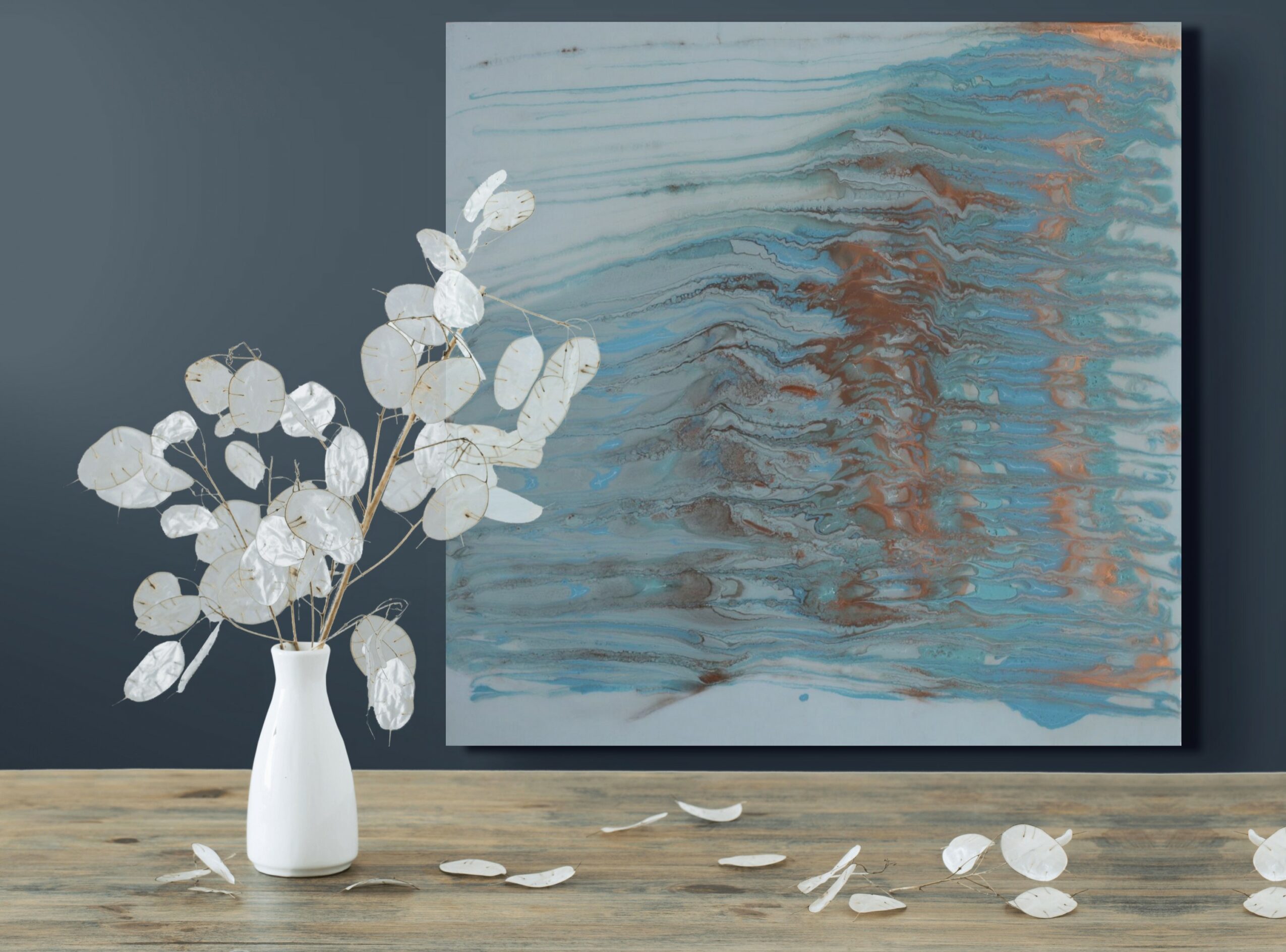 Vase with white flowers and an abstract painting on a wall, with petals scattered on the wooden surface.