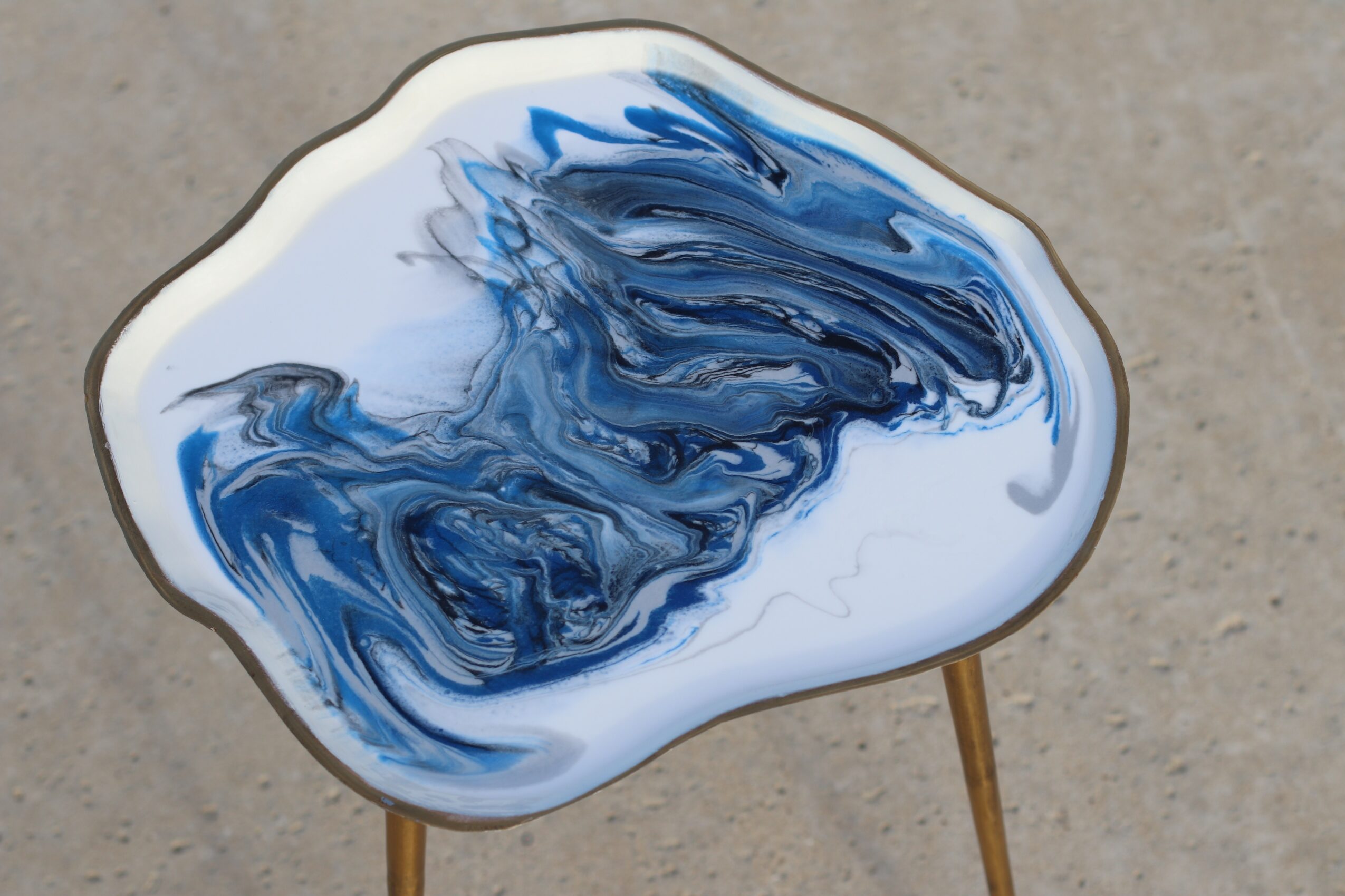 Round table with a blue and white marbled pattern top and three wooden legs, on a concrete surface.