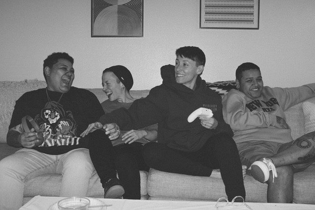 Four people sitting on a couch, laughing and talking, in a living room with framed artwork on the wall.