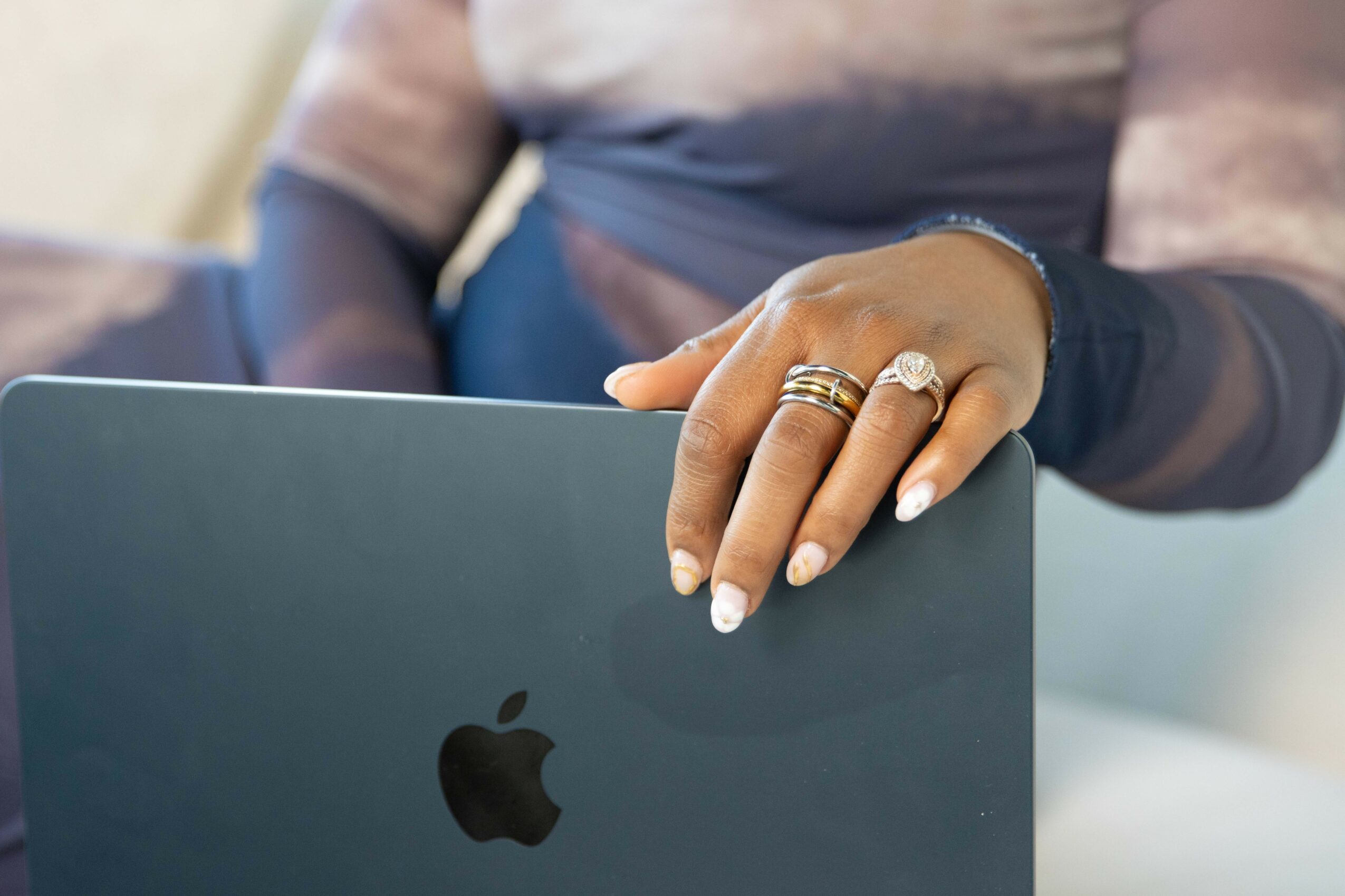 Person's hand resting on a laptop with rings on fingers, background blurred.