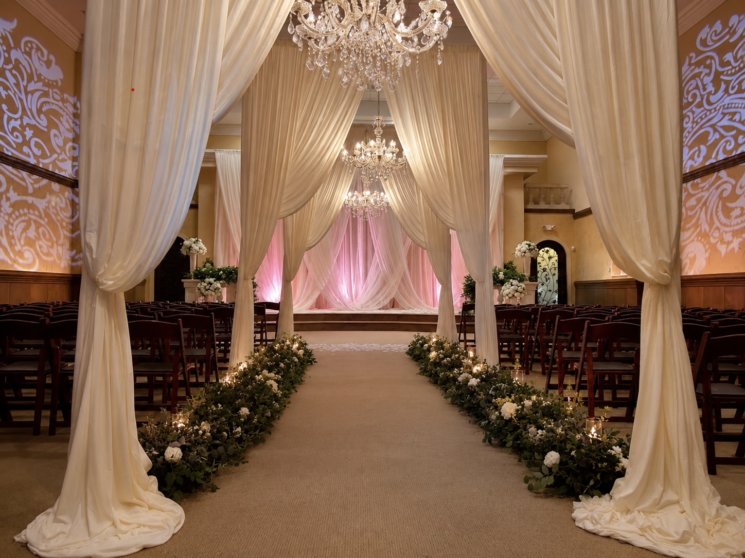 Elegant wedding ceremony setup with draped curtains, chandeliers, and floral aisle decorations, viewed from the entrance. Word count: 20.