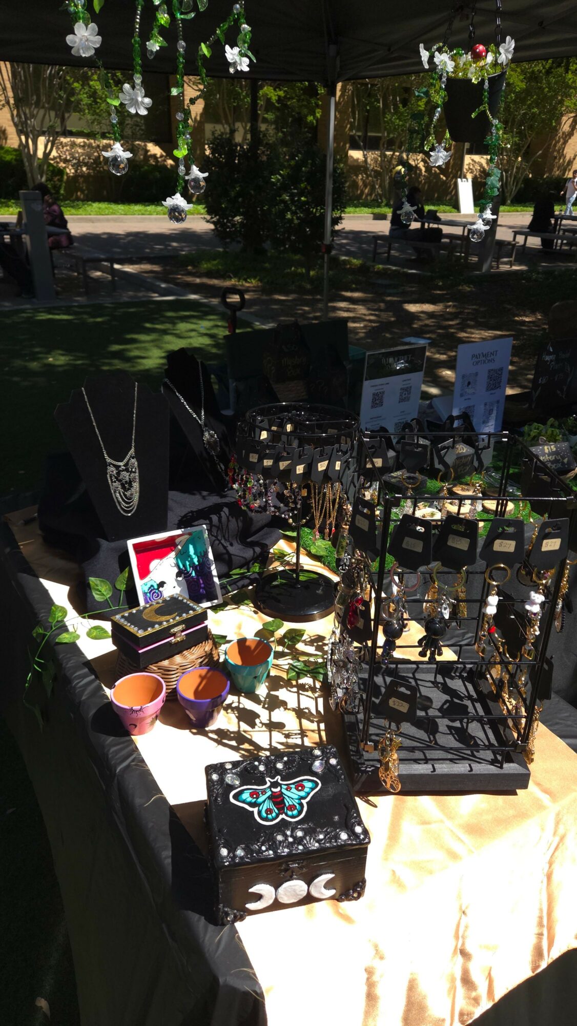 Outdoor display with various items on tables, including framed pictures, a black bag, and decorative objects, under trees.