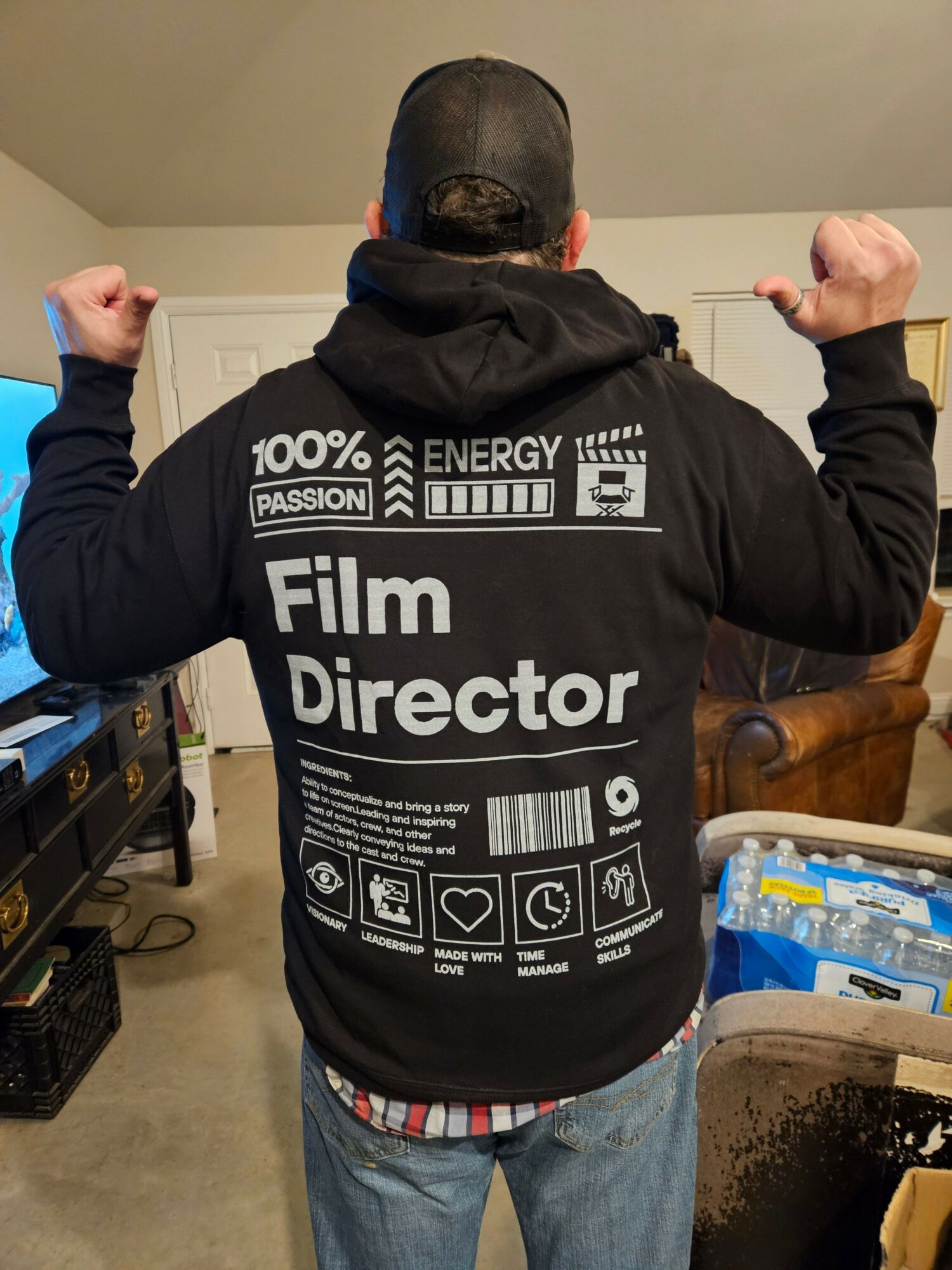 Person wearing a black jacket with film-related icons and text, standing indoors with arms raised, back facing the camera.