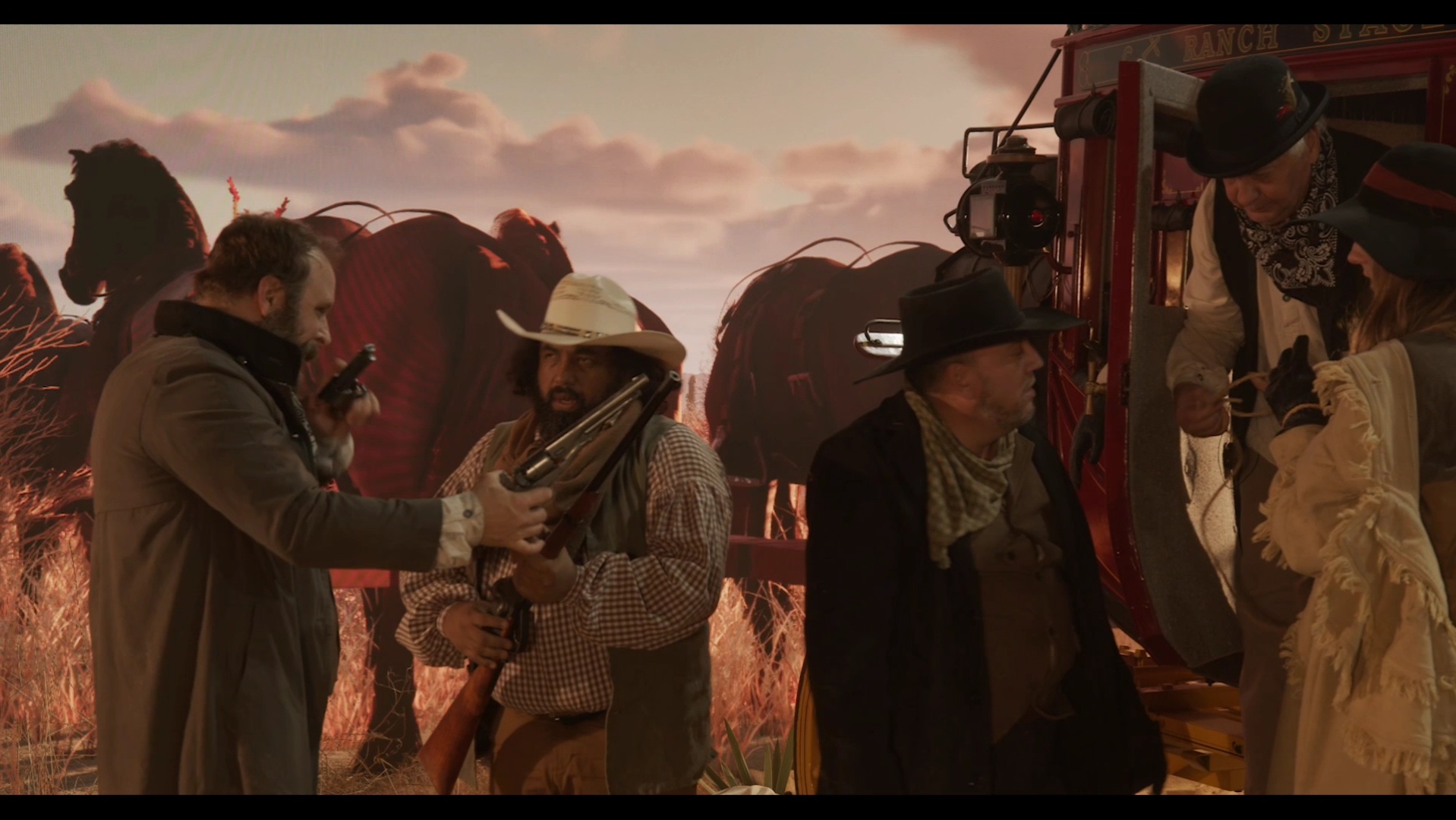Group of people in period clothing outdoors with horses and a wagon at sunset.