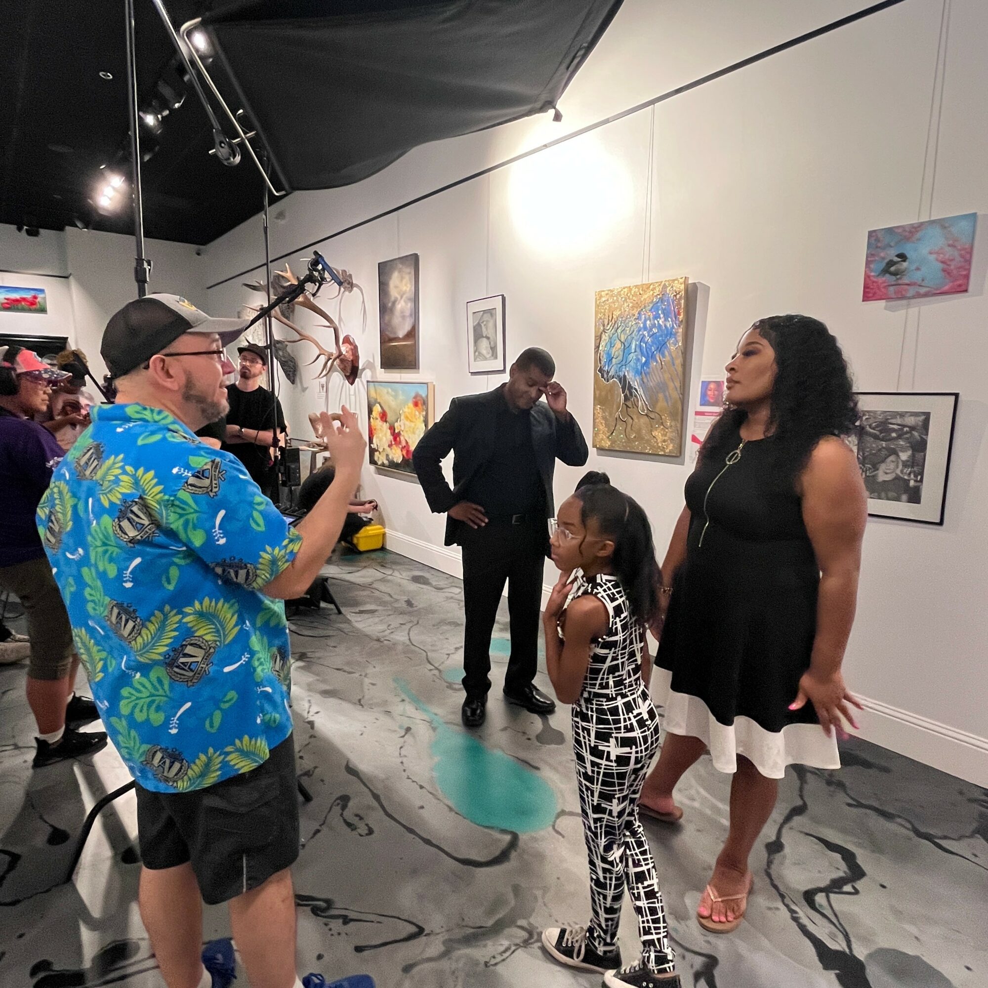 Group of people in an art gallery, some talking and others observing paintings on the wall.