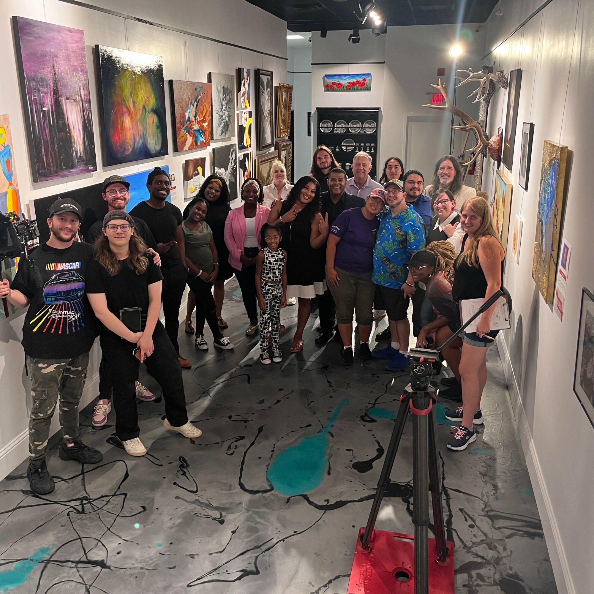 Group of people in an art gallery with colorful paintings on walls, some smiling and looking at the camera.