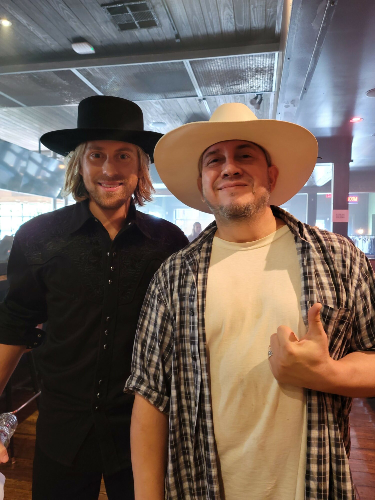 Two people wearing hats and casual clothing, standing indoors with a modern background.