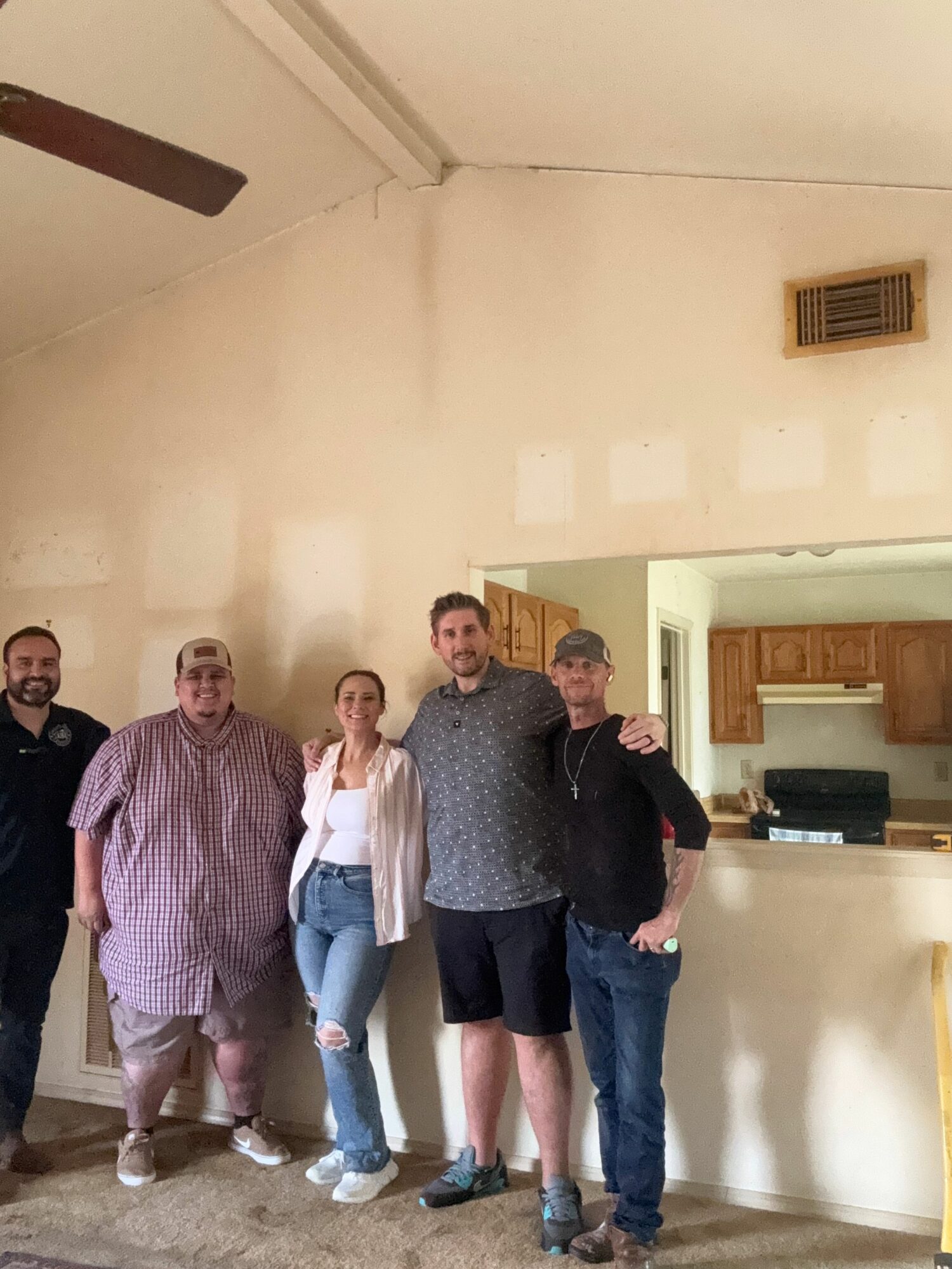 Four people standing in a room with a kitchen in the background, smiling and posing for the photo.