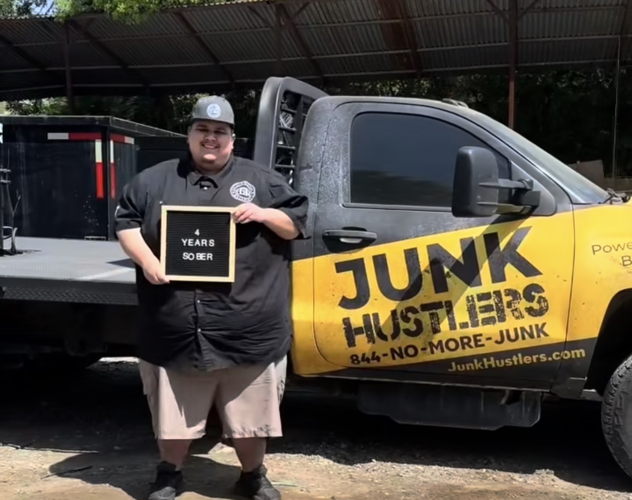 Person holding a plaque standing next to a yellow and black junk removal truck outdoors.