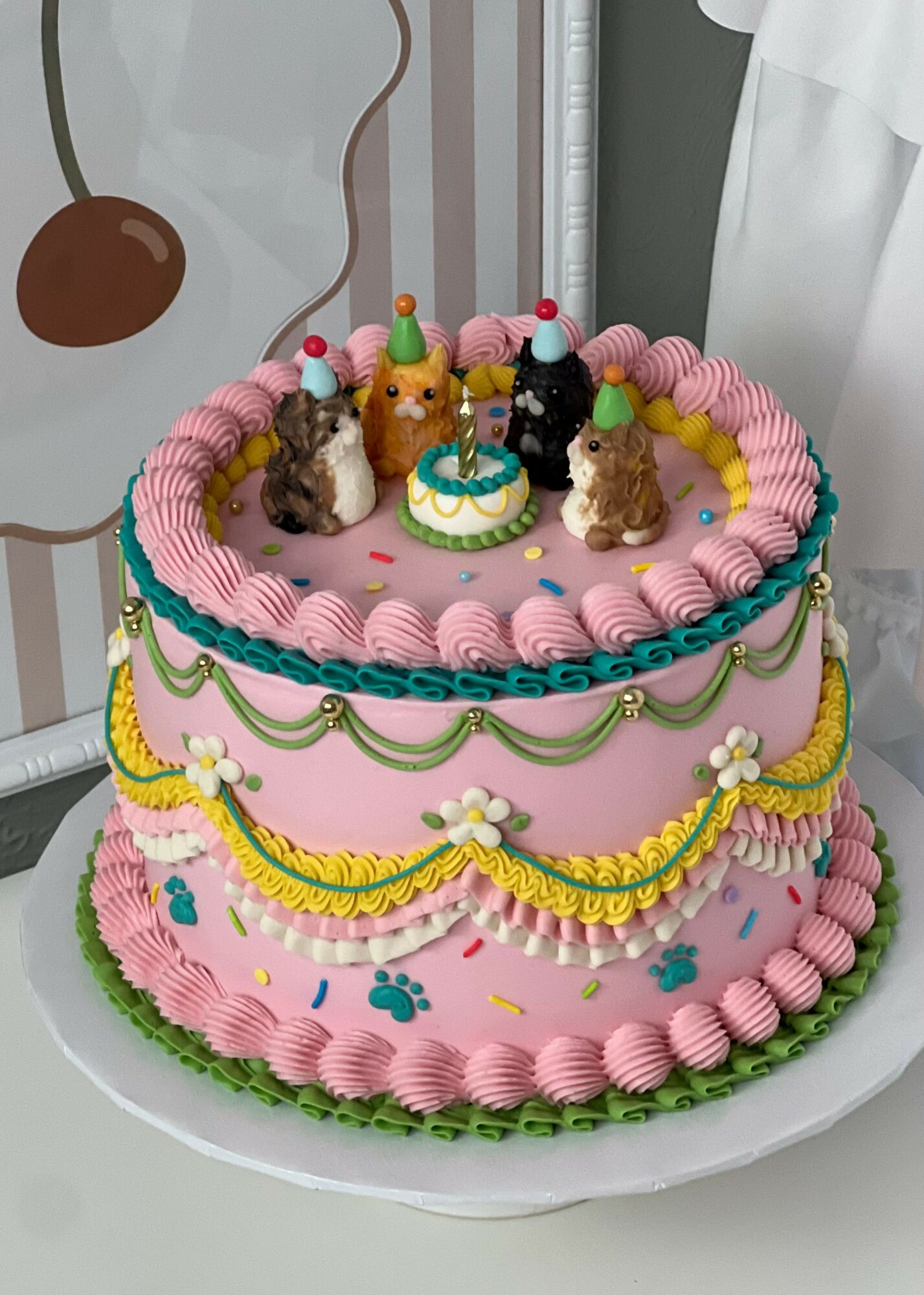 Decorated birthday cake with small animal figurines, pink and yellow frosting, and colorful sprinkles, on a white cake stand.