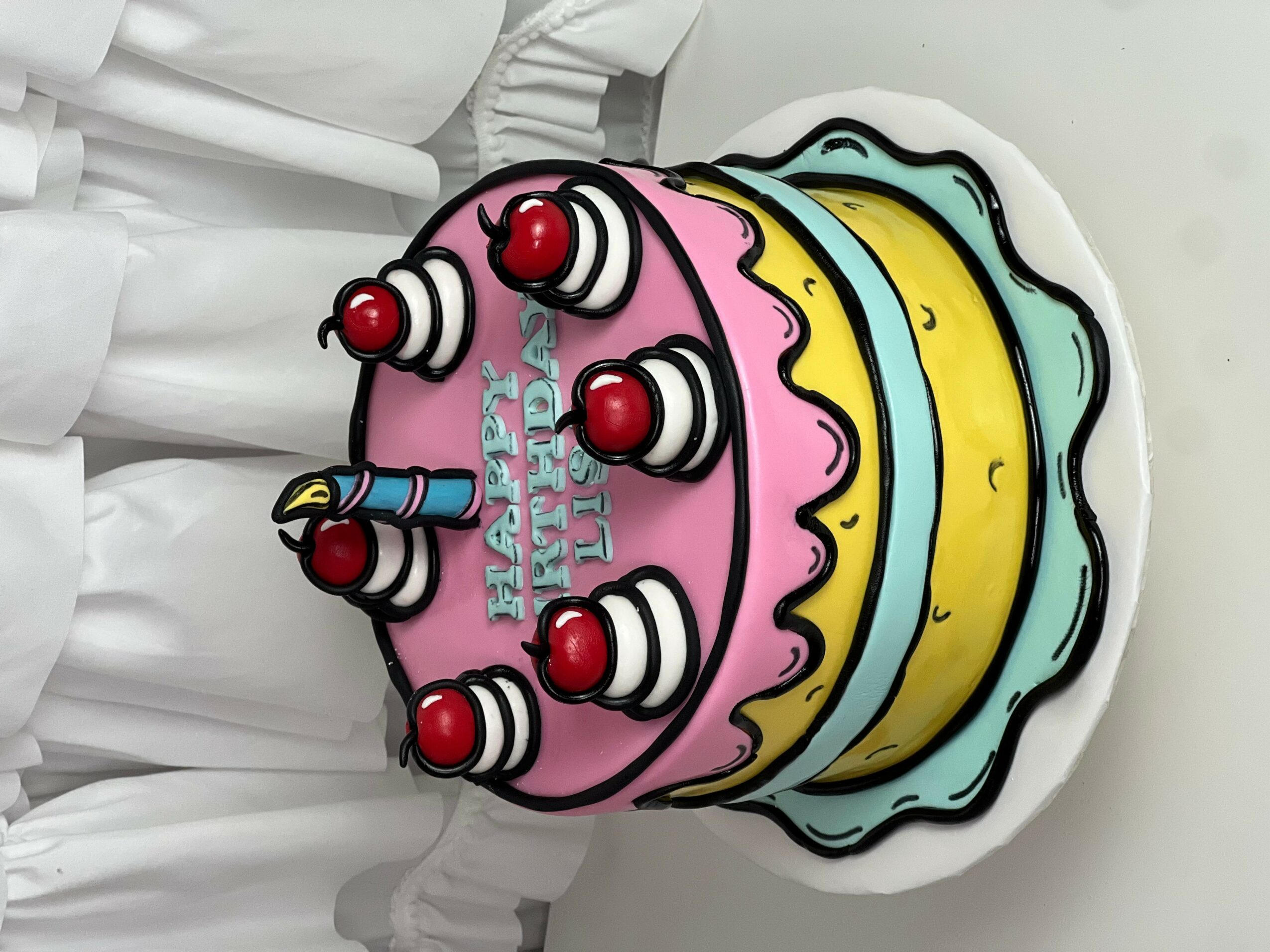 Colorful birthday cake with pink, yellow, and blue layers, decorated with red cherries and a birthday message, on a white background.