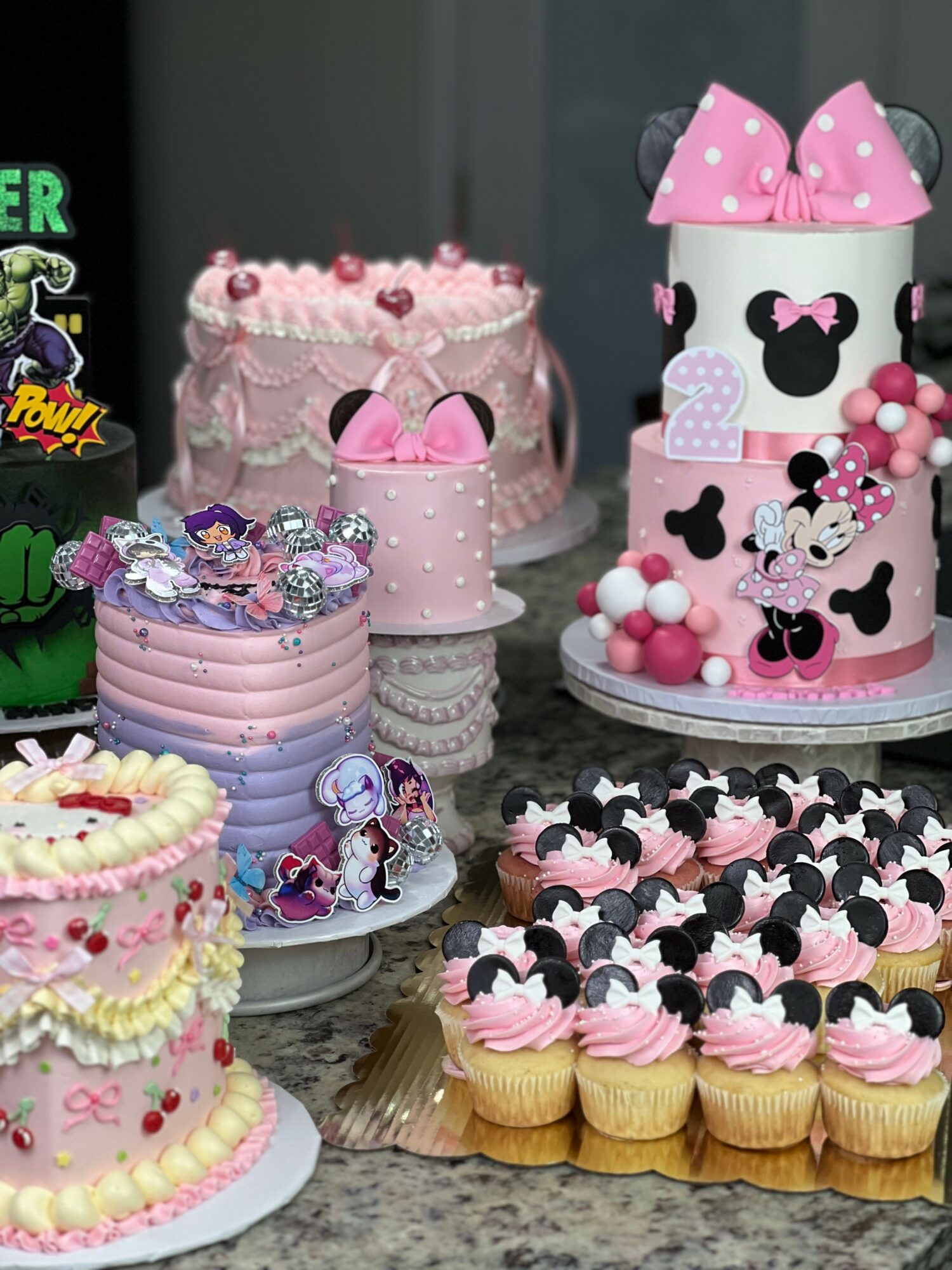 Assorted decorated cupcakes and a pink themed cake with Minnie Mouse design on a table.