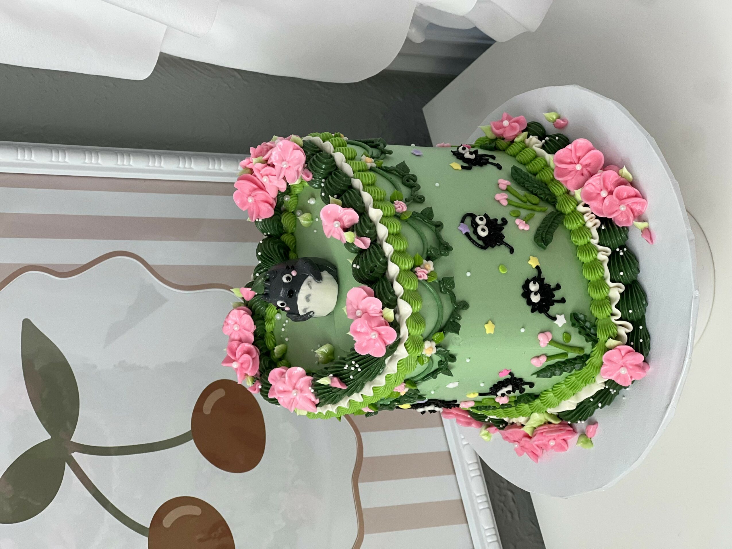 Decorative cake with green icing, pink flowers, and black and white accents, displayed on a white surface.