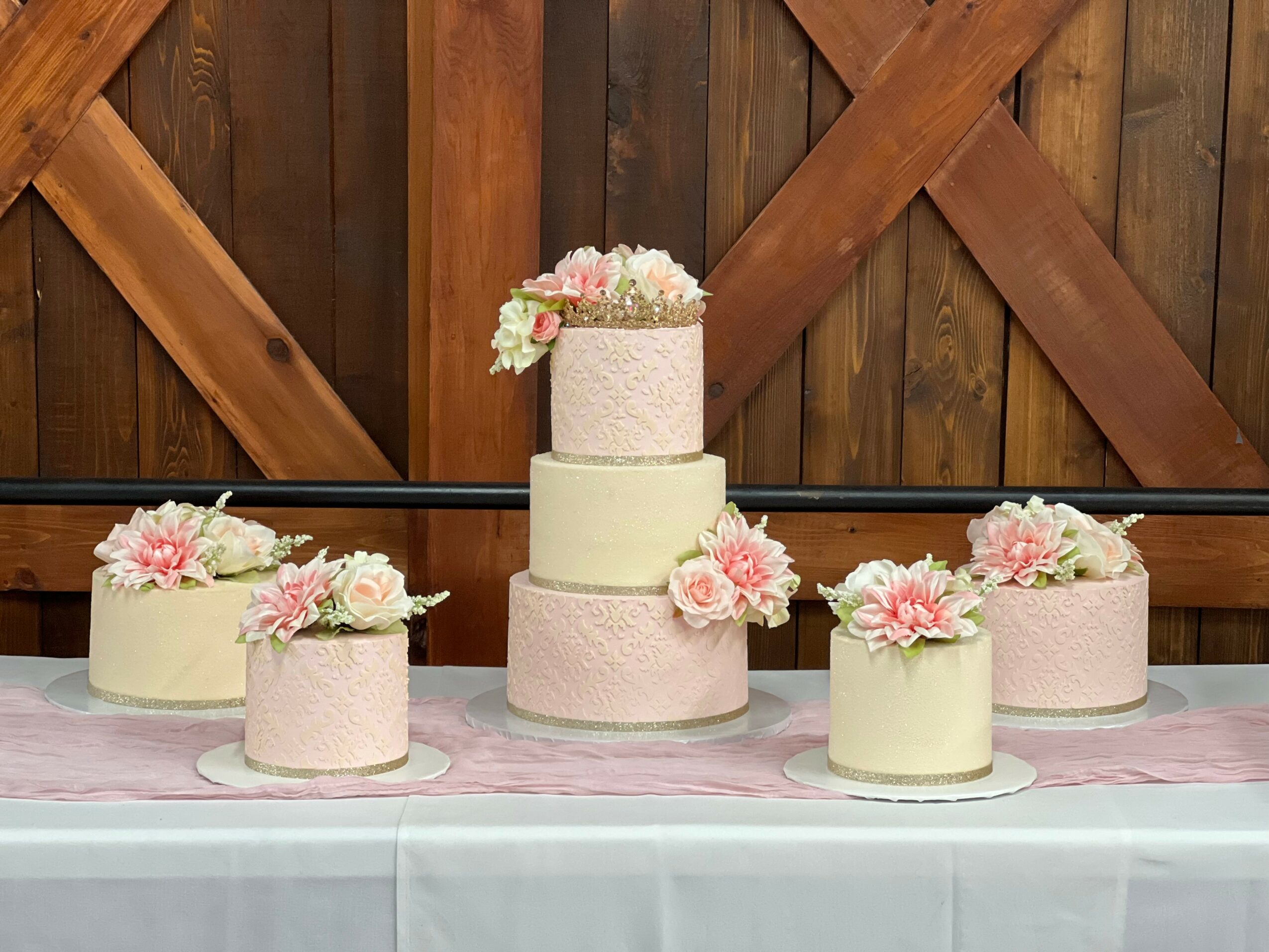 Six layered cakes decorated with pink and white flowers on a table with a wooden fence background.