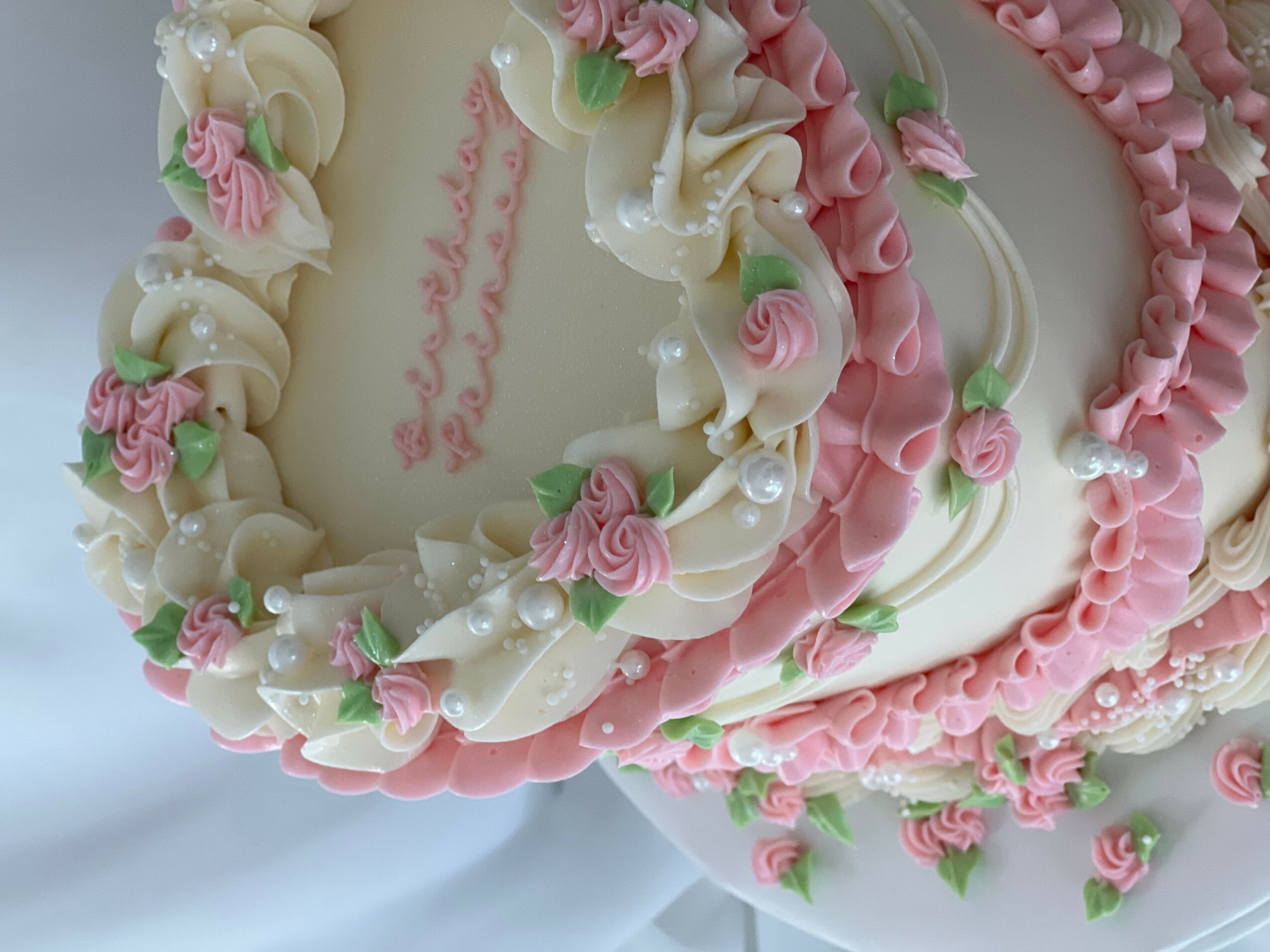 Decorative cake with pink and white icing flowers and ruffles, featuring a message written in pink icing.