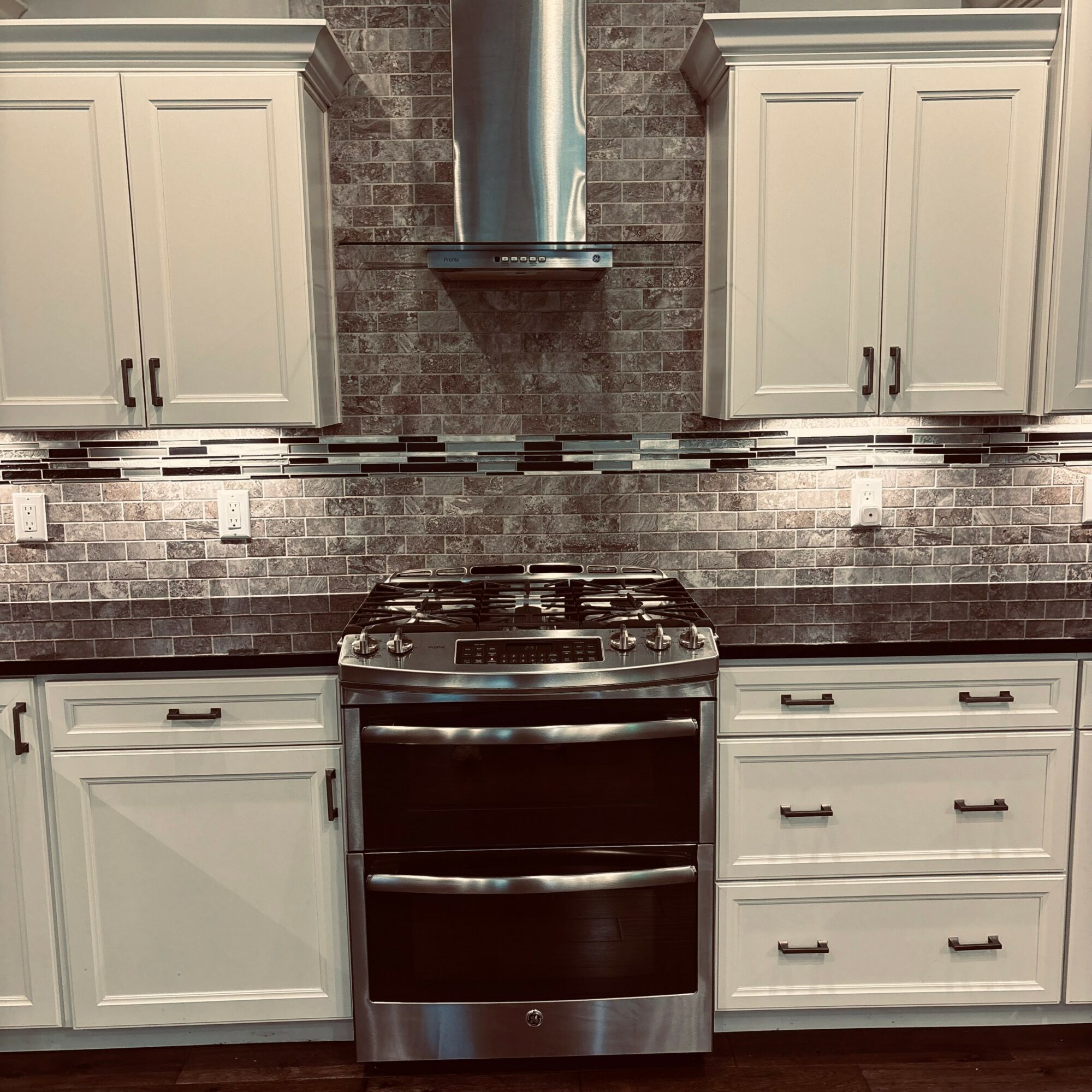 Kitchen with white cabinets, a stainless steel stove, and a brick backsplash, centered under a range hood.