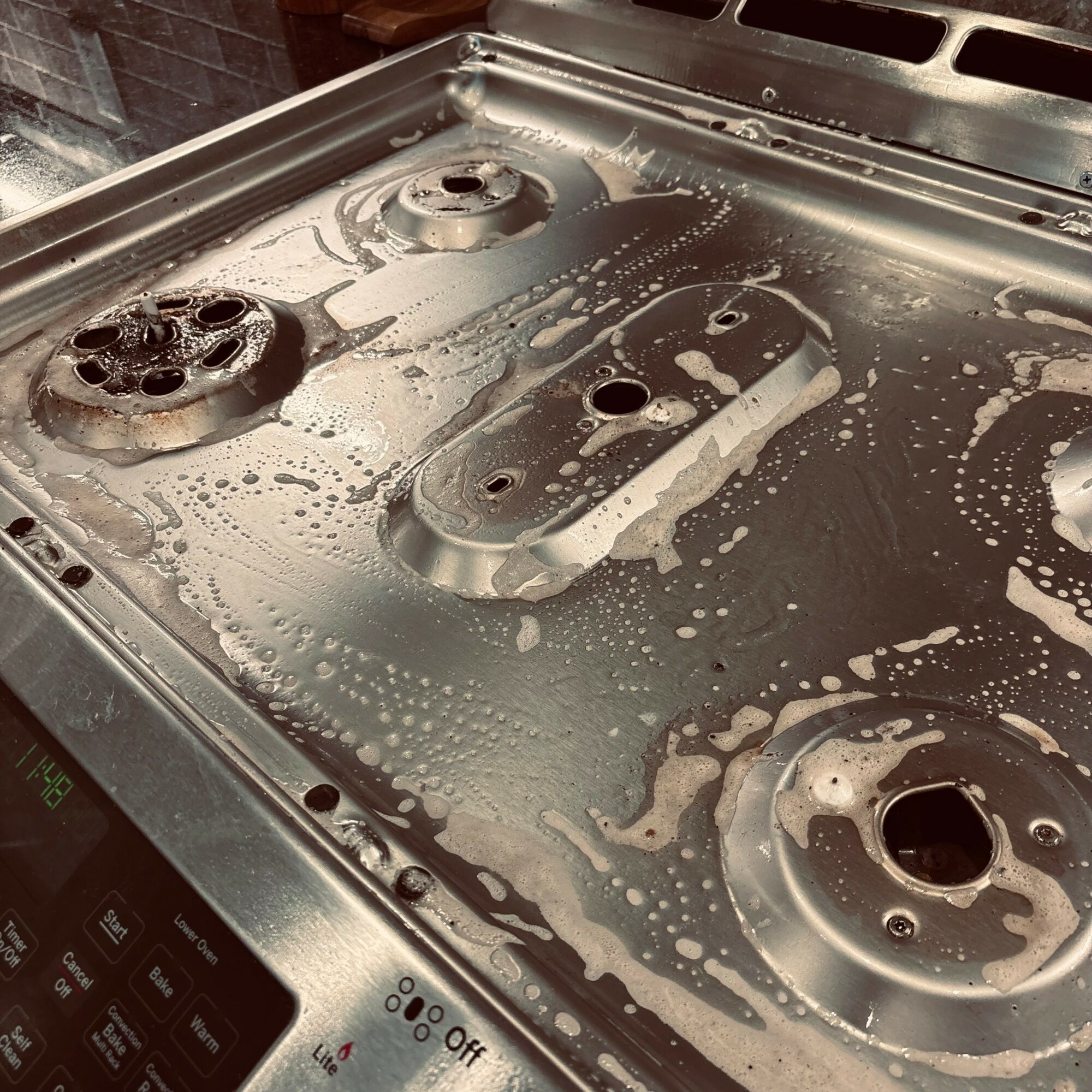 Stovetop with four burners covered in soap suds and water, with control panel visible at the bottom left corner.