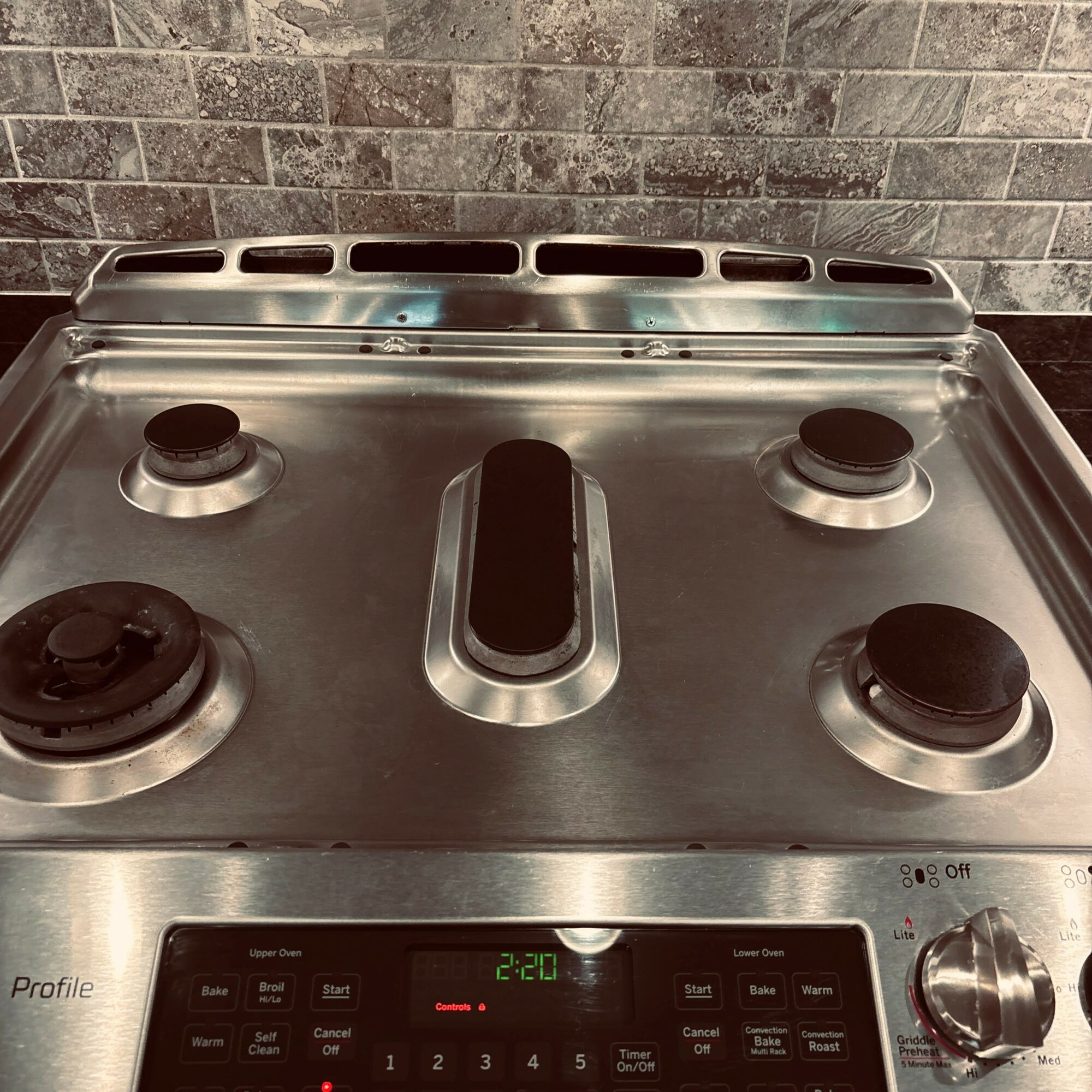 Stainless steel gas stove with four burners and control knobs, against a brick wall background.